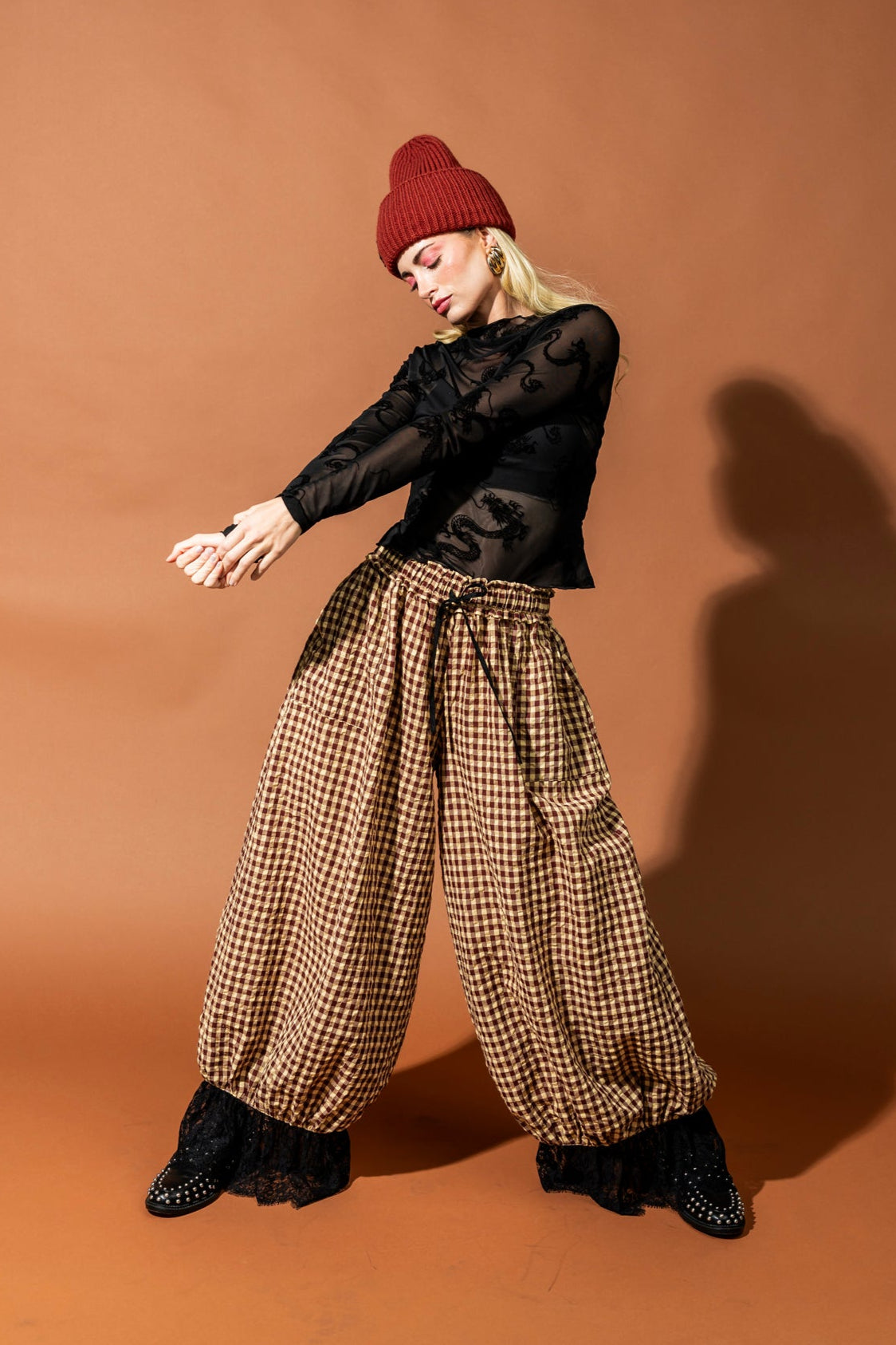 Person wearing a black top and checkered pants with a red beanie on a brown background