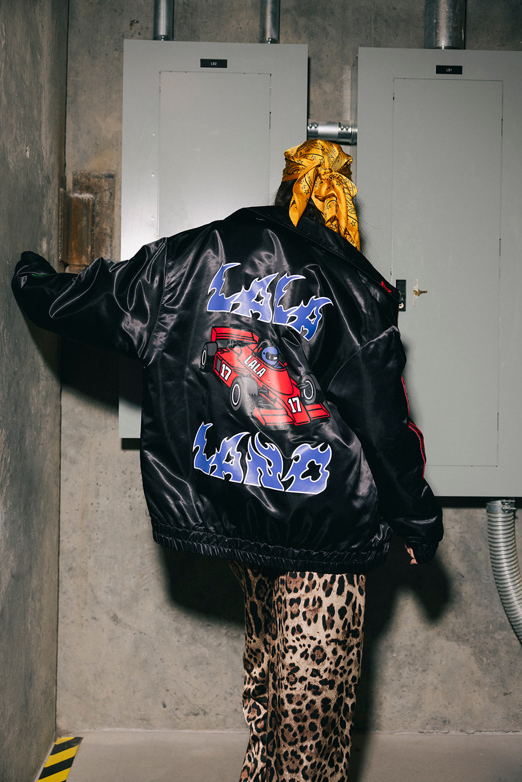 Person wearing a black jacket with colorful graphics and leopard print pants in an industrial setting.