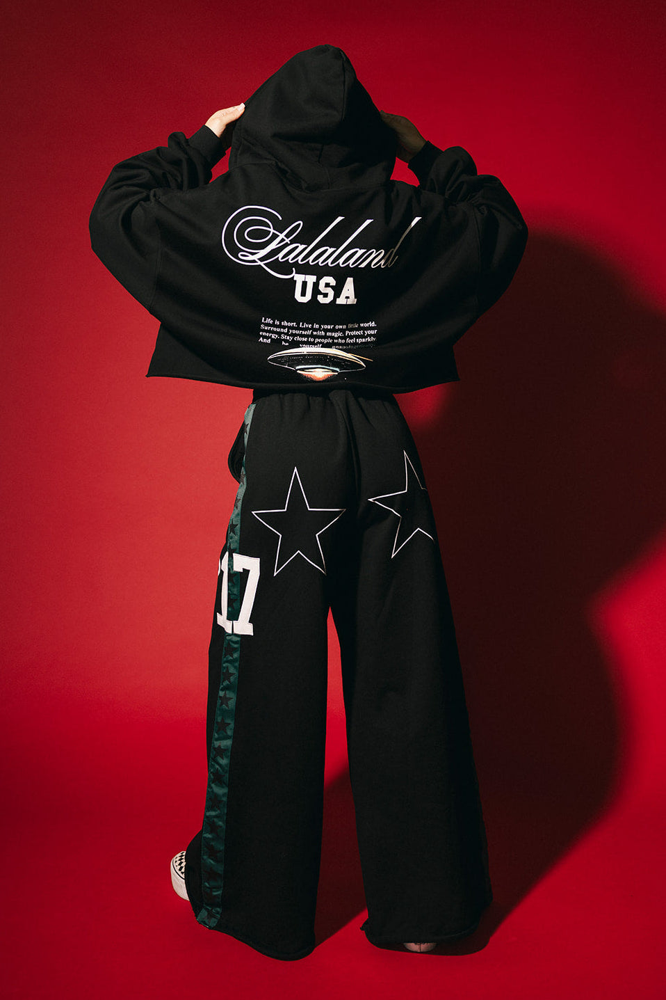 Person wearing a black hoodie and pants with visible branding on a red background