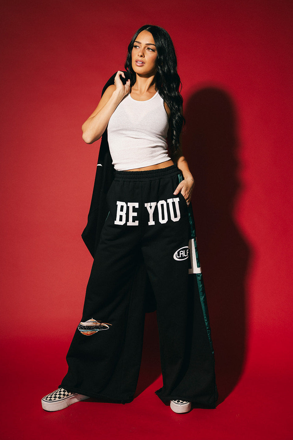 Woman wearing a white top and black pants with 'BE YOU' text on a red background