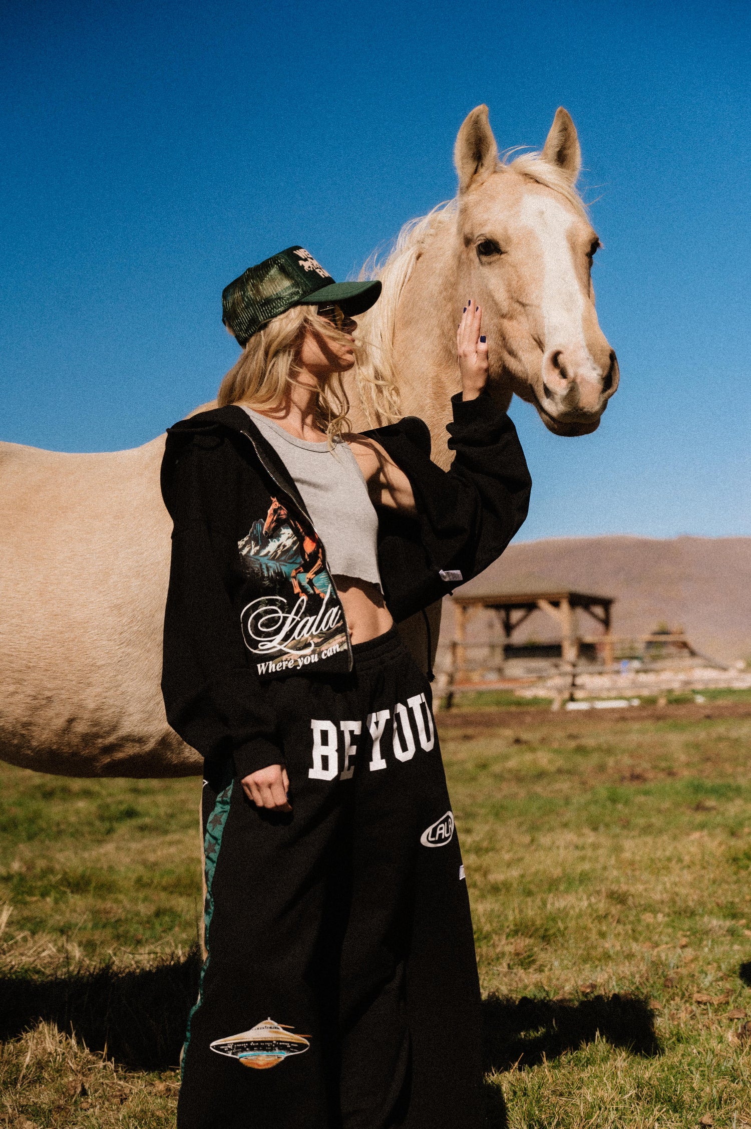 Person wearing a black hoodie with visible branding, standing next to a horse in an outdoor setting.