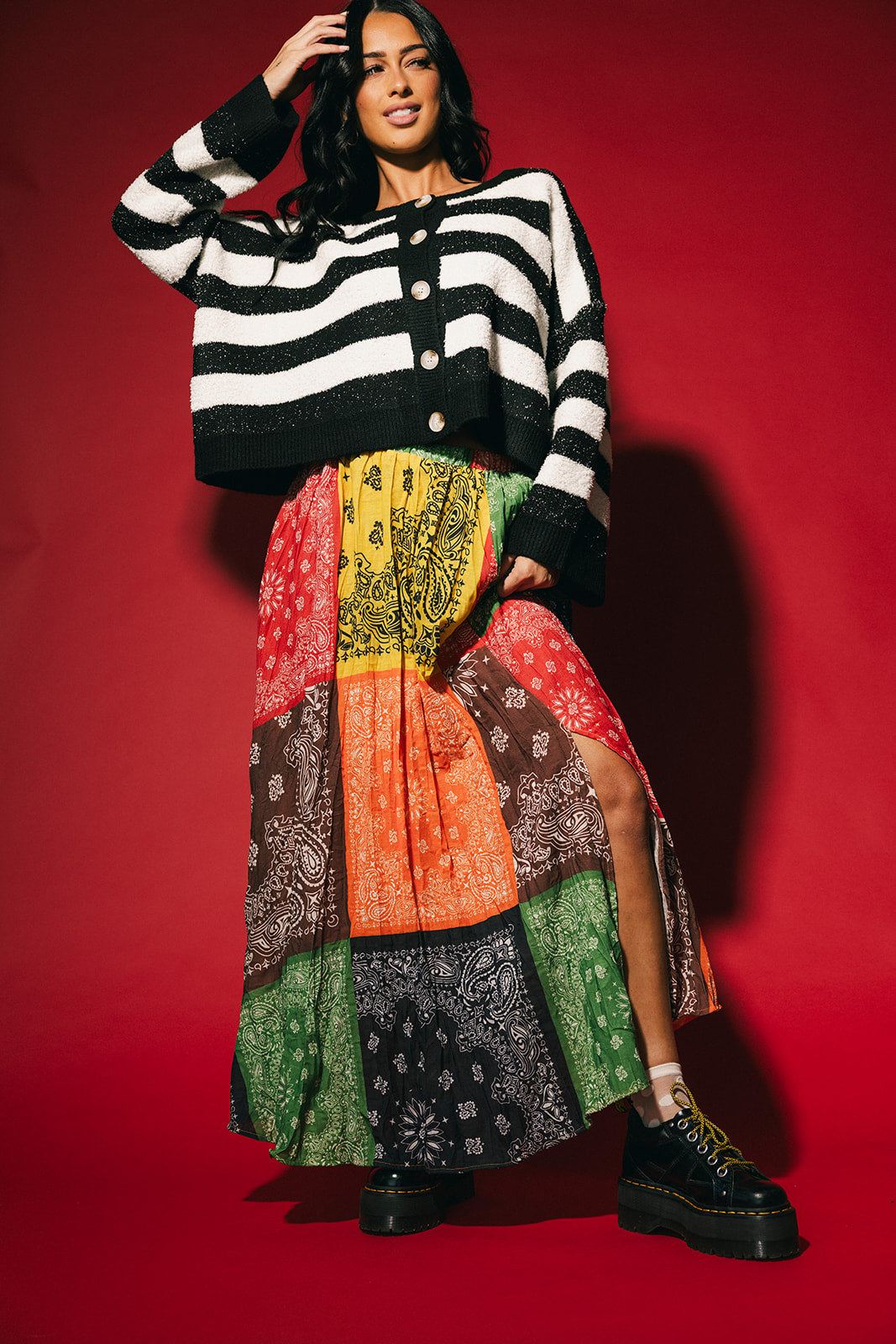 Woman wearing a patchwork style bandana print pleated midi skirt with a side slit on a red background