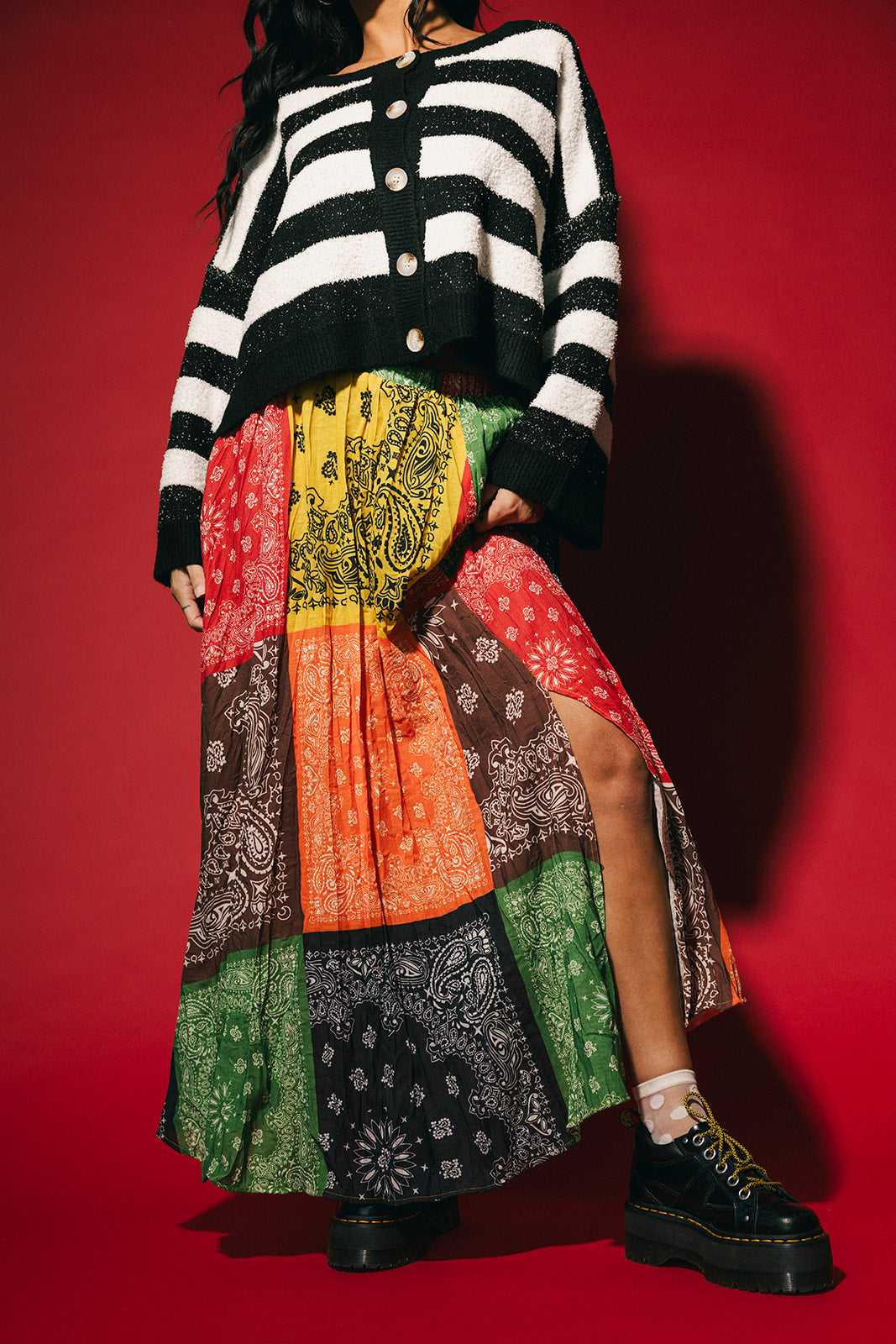 Person wearing a patchwork style bandana print pleated midi skirt with a side slit on a red background