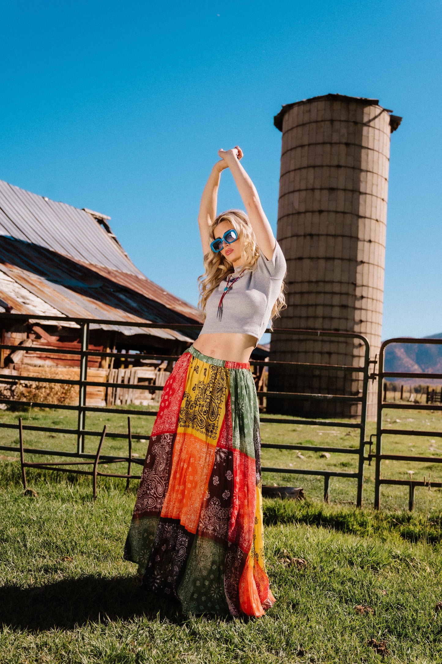 Woman in a patchwork style bandana print pleated midi skirt standing in a rural setting with a silo and barn in the background.