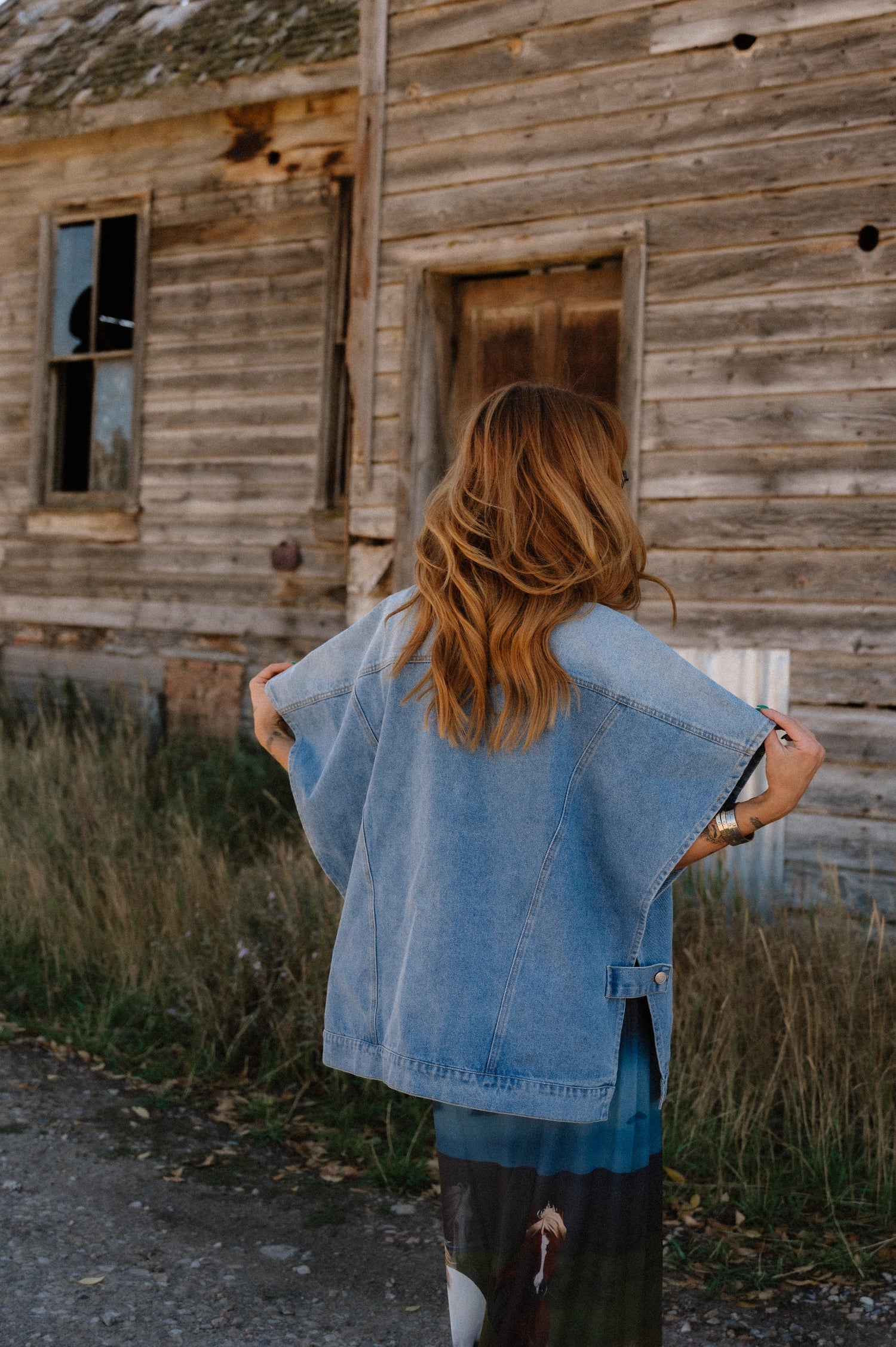 Person wearing a denim jacket standing in front of an old wooden building