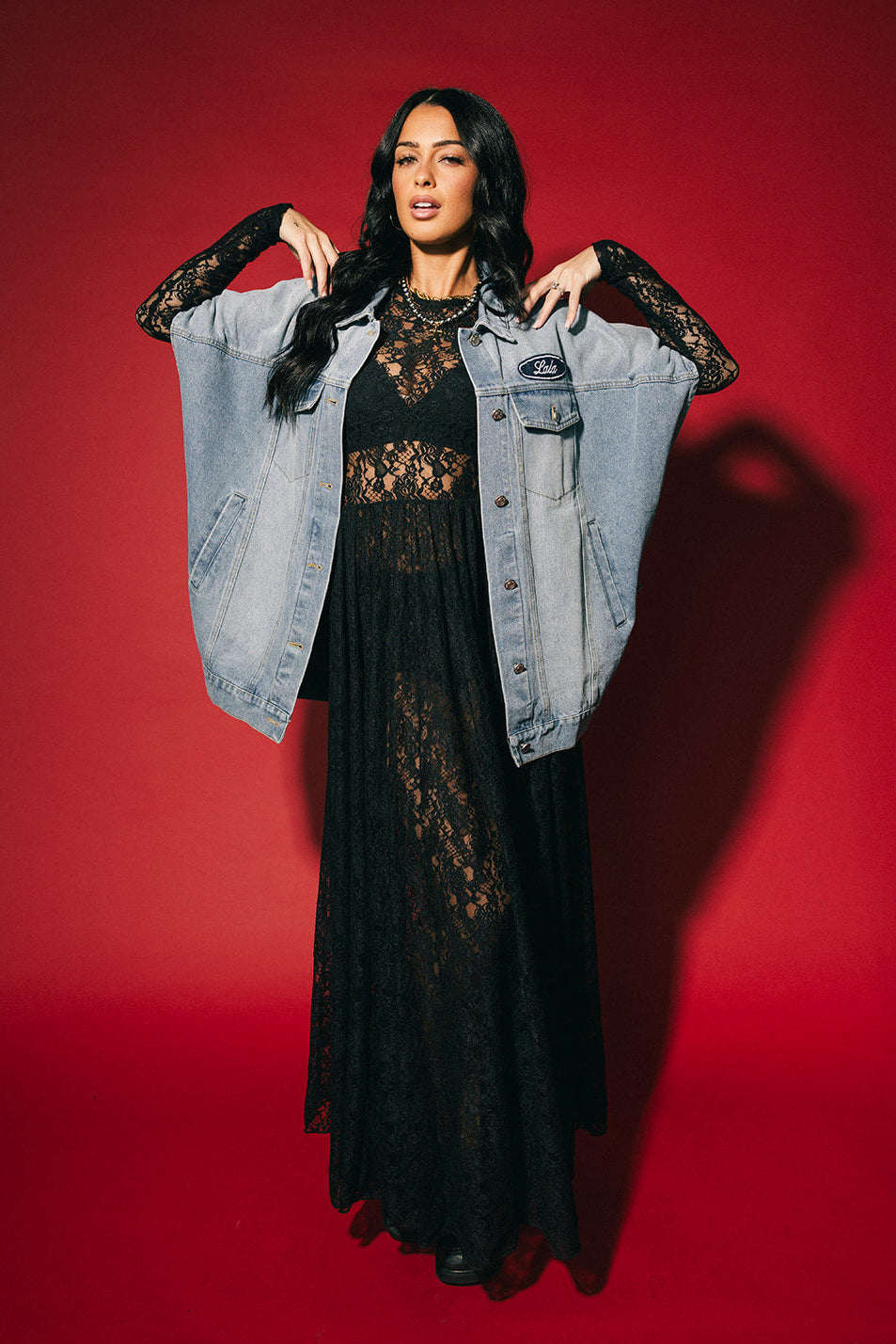 Woman wearing a black lace dress with a denim jacket against a red background