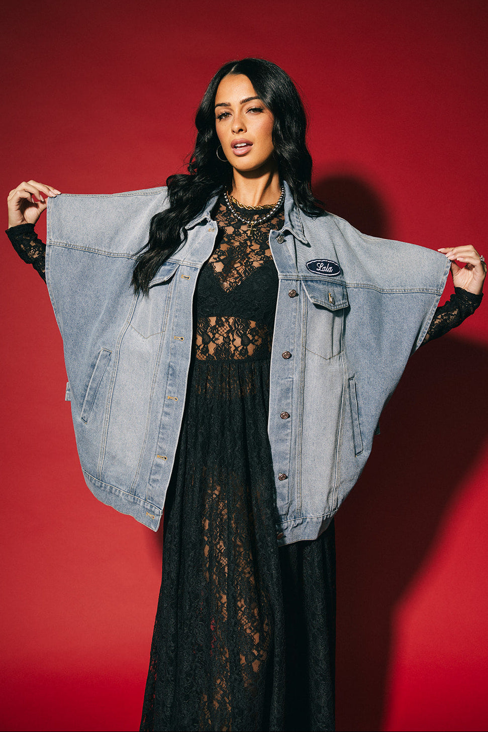 Woman wearing a black lace dress with a denim jacket against a red background