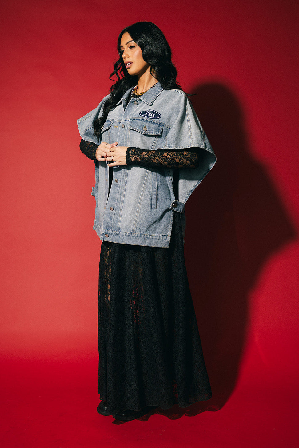 Woman wearing a denim jacket over a black dress against a red background