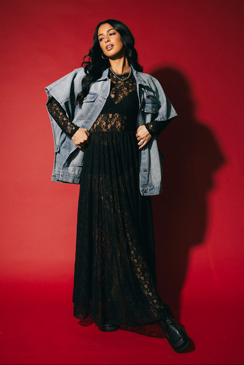 Woman wearing a black lace dress with a denim jacket against a red background