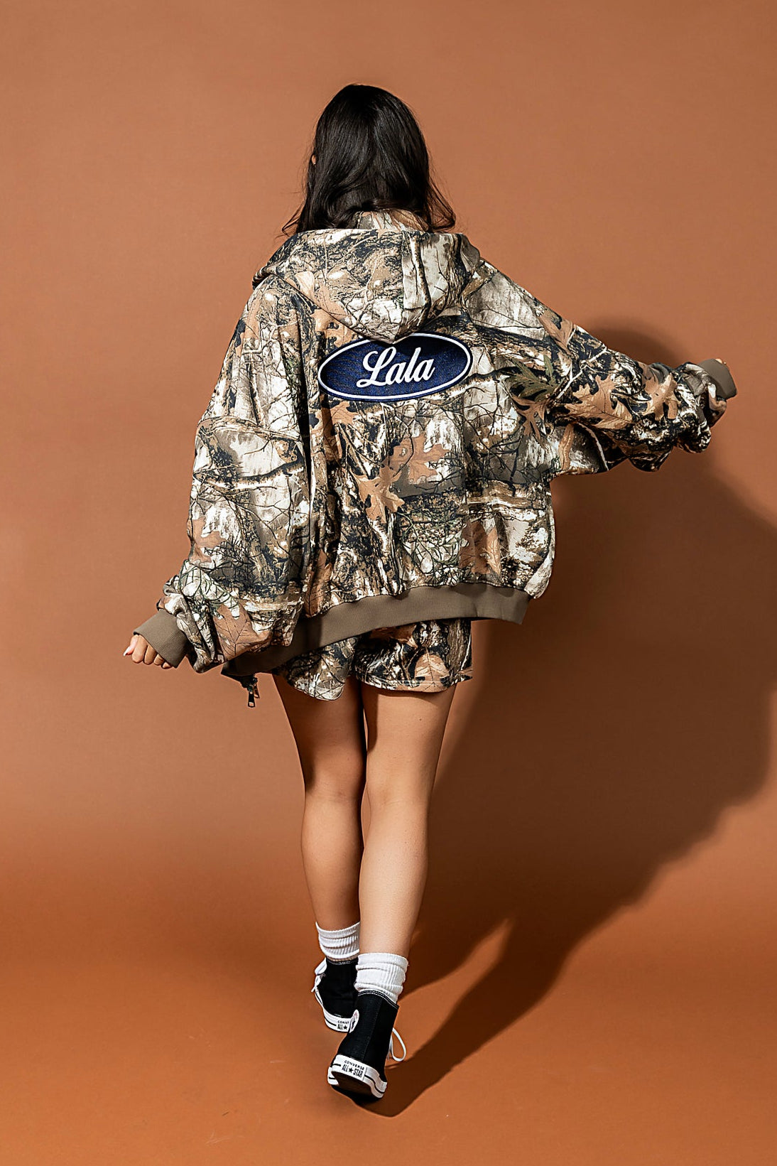 Person wearing a camouflage jacket with 'Lala' branding on a brown background