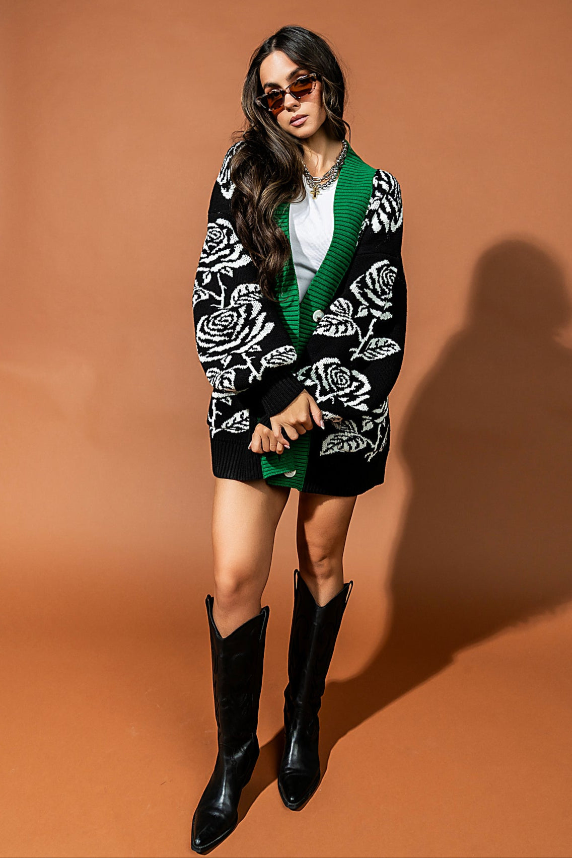 Woman wearing a patterned cardigan and black boots against a brown background