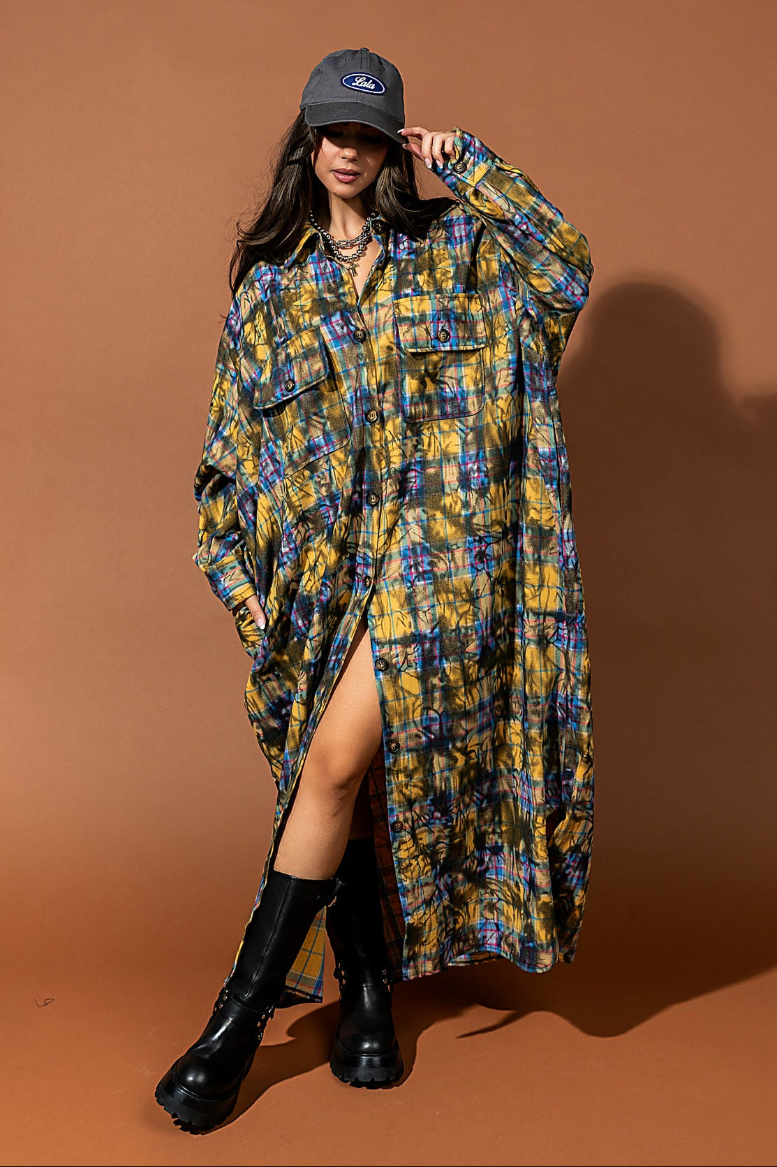 Woman wearing a long, patterned shirt dress with black boots against a brown background