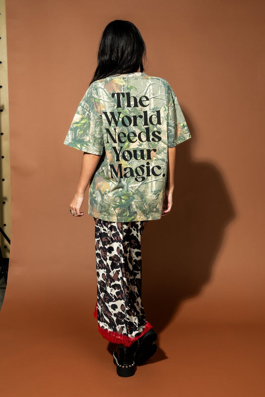 The World Needs Your Magic Real Tree Camo Tee - girl weating oversized camo tee with black smile face on the front and "the world needs your magic" on the back