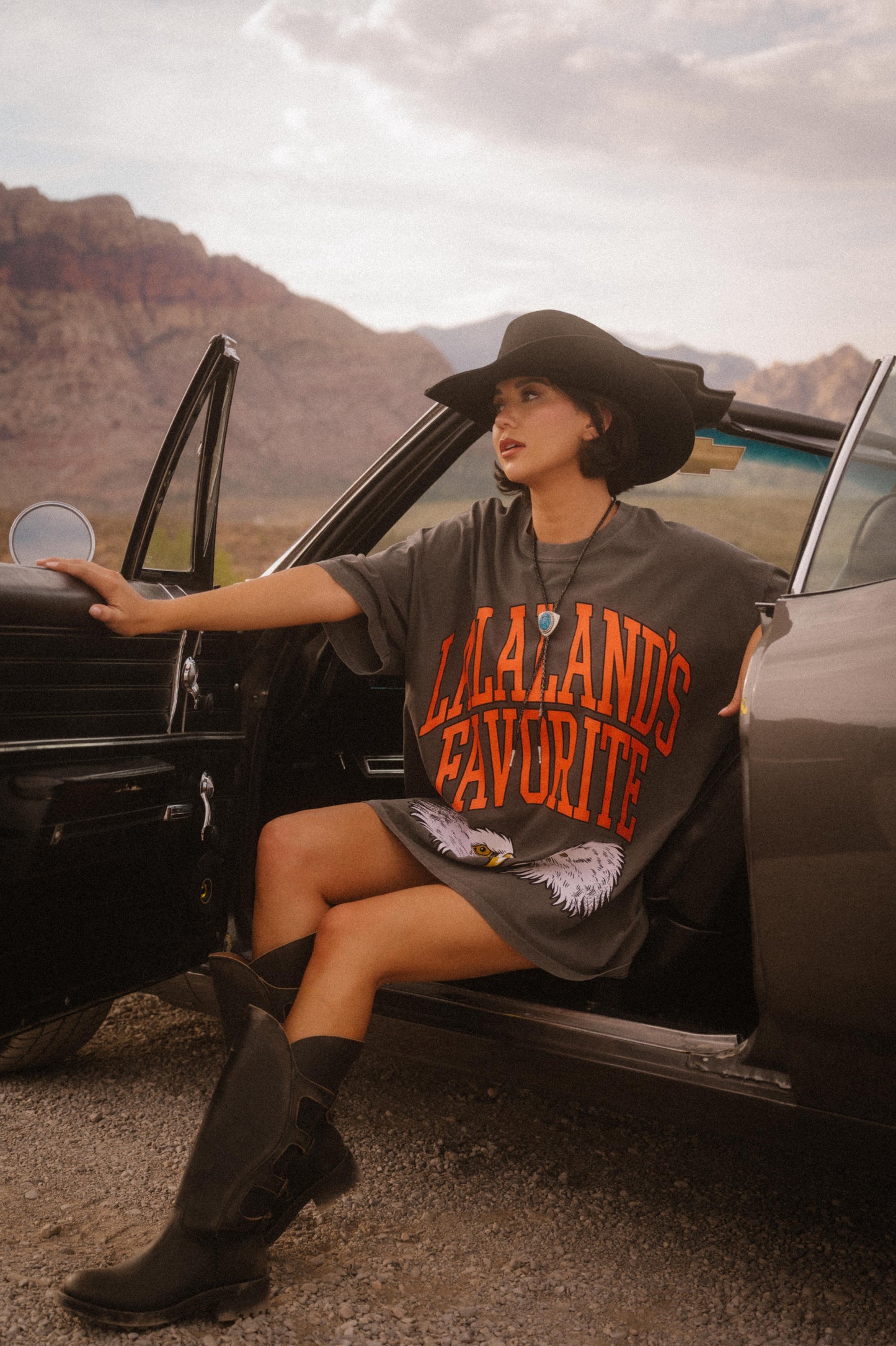 Person wearing a shirt with 'Lalaland's Favorite' text, sitting in an open car door outdoors.