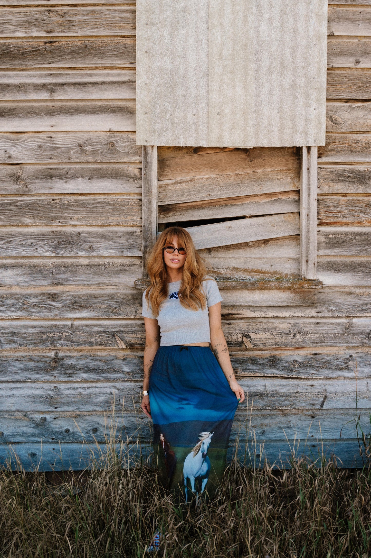 Woman standing in front of a wooden wall wearing a blue skirt with a horse design.