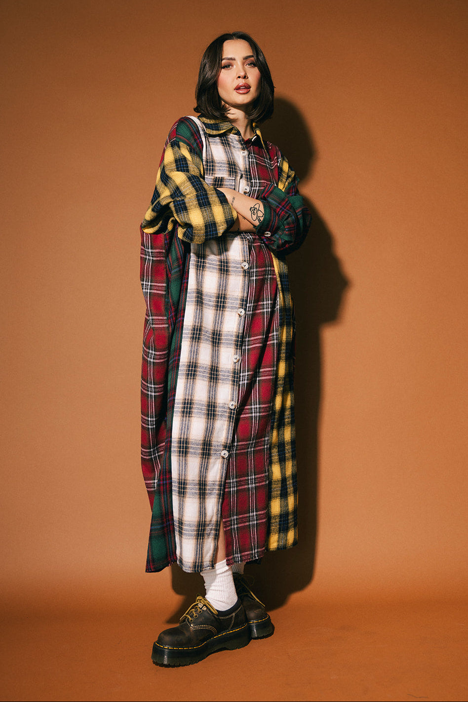 Person wearing a long patchwork plaid dress against a brown background