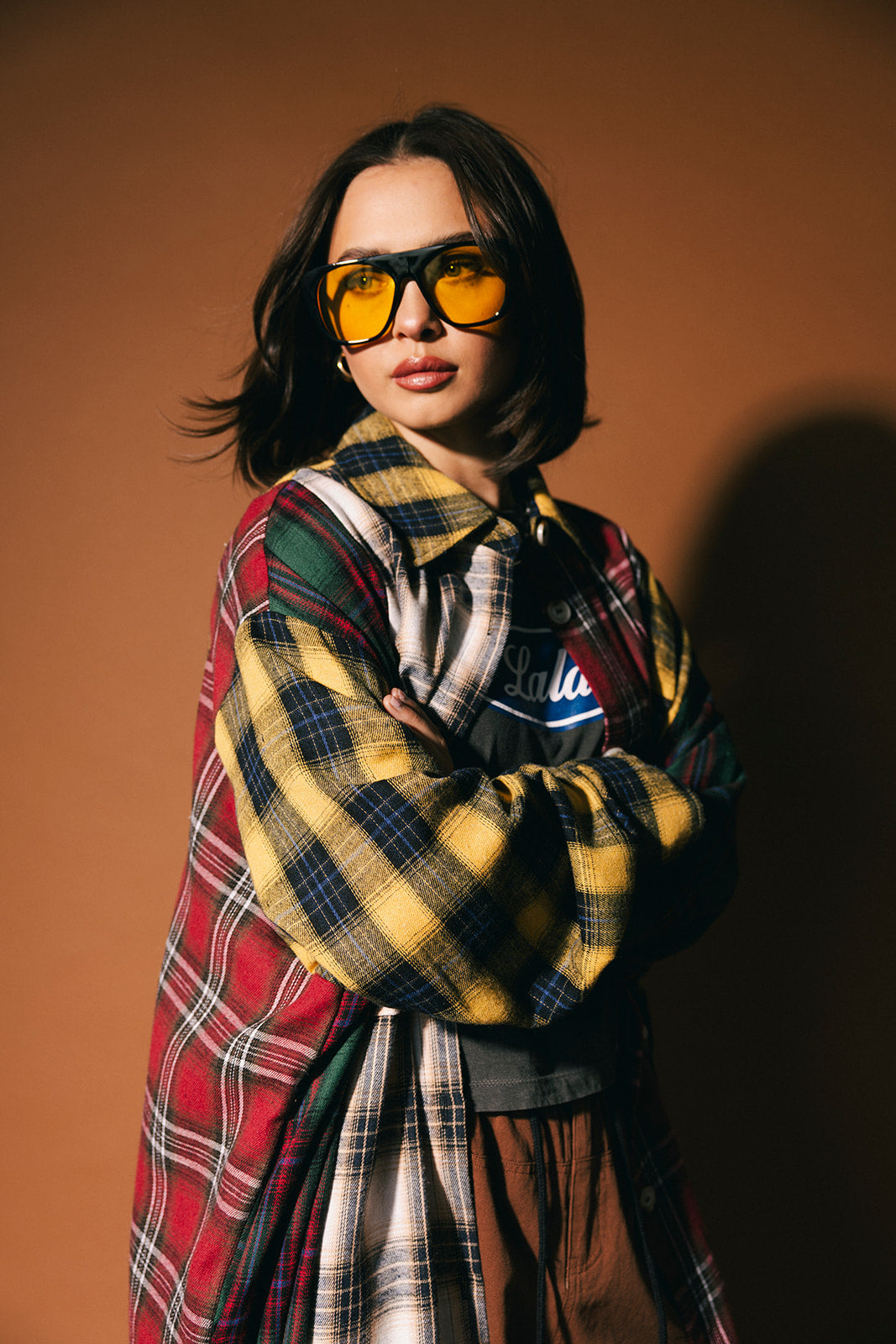 Woman wearing a patchwork plaid duster and sunglasses against a brown background
