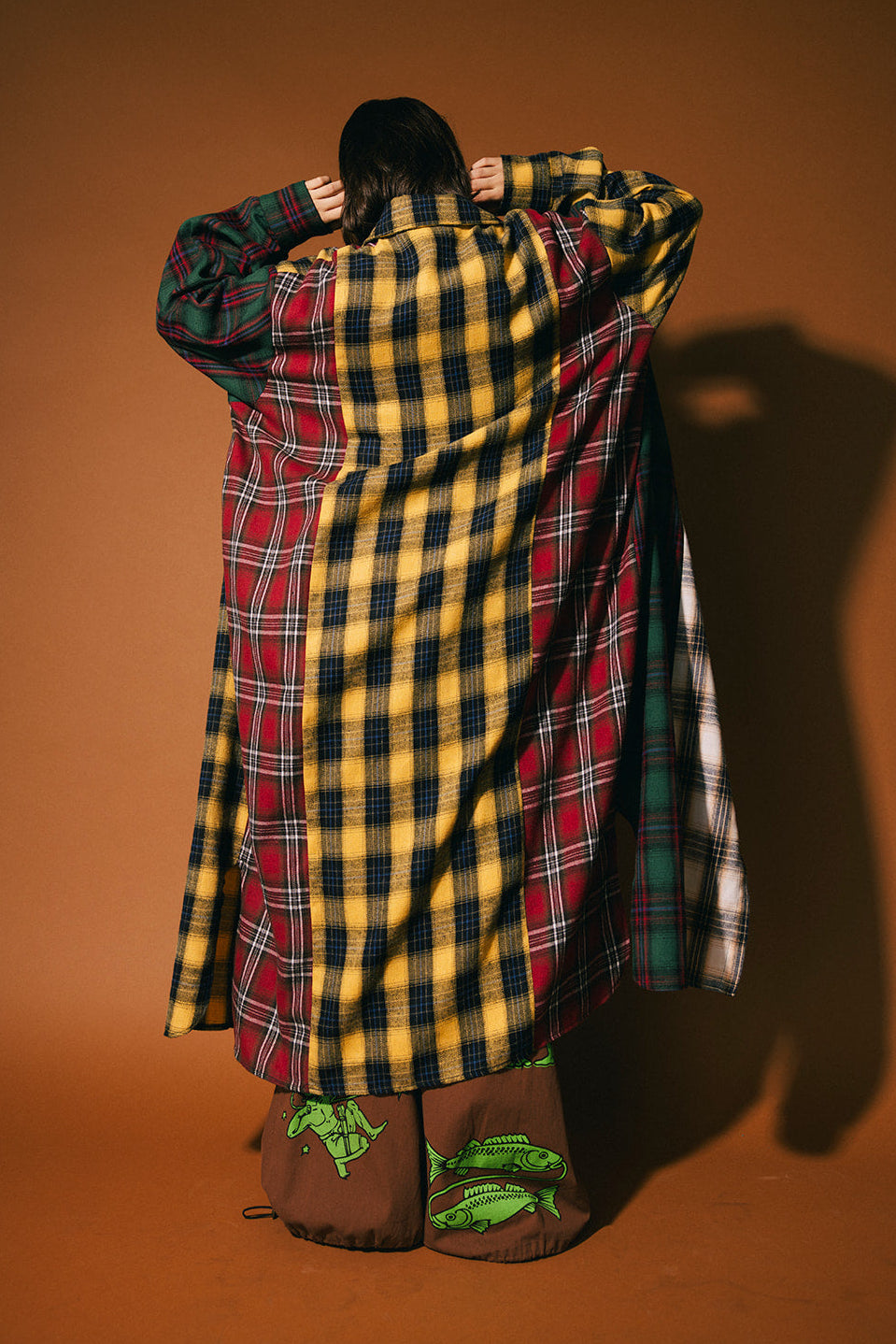 Person wearing a long, patchwork plaid duster on a brown background