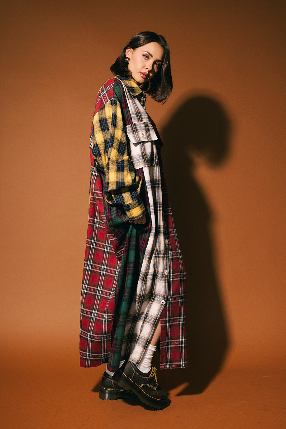 Woman wearing a long patchwork plaid dress against a brown background