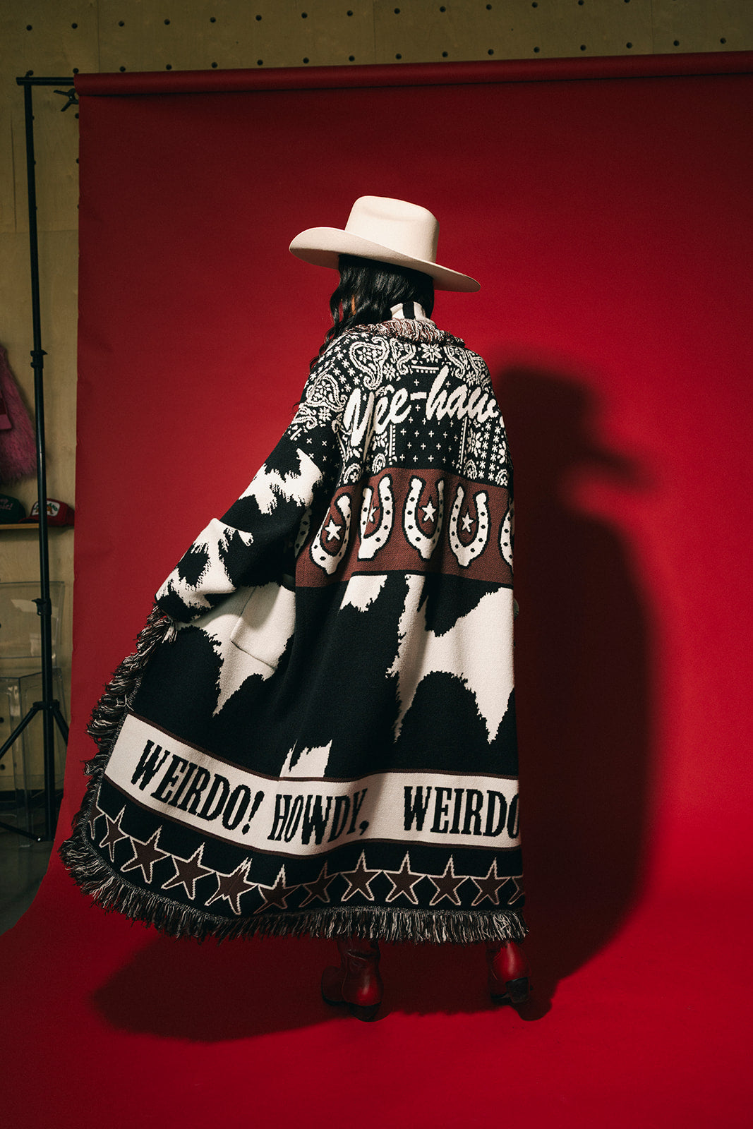 Person wearing a patterned cardigan with text and a cowboy hat against a red background