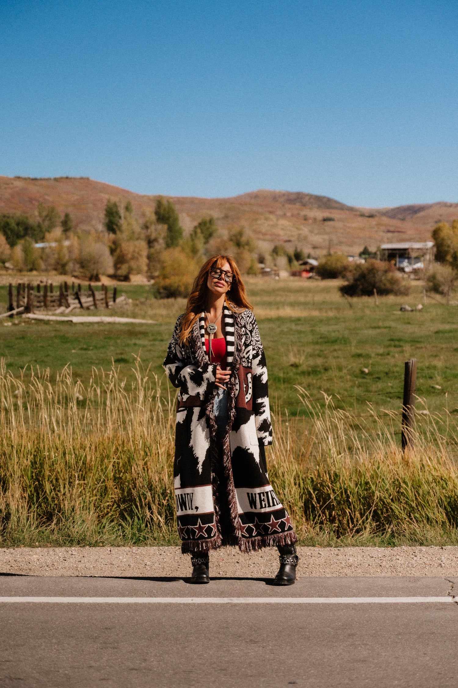 Person standing on a road with a scenic background of mountains and fields.