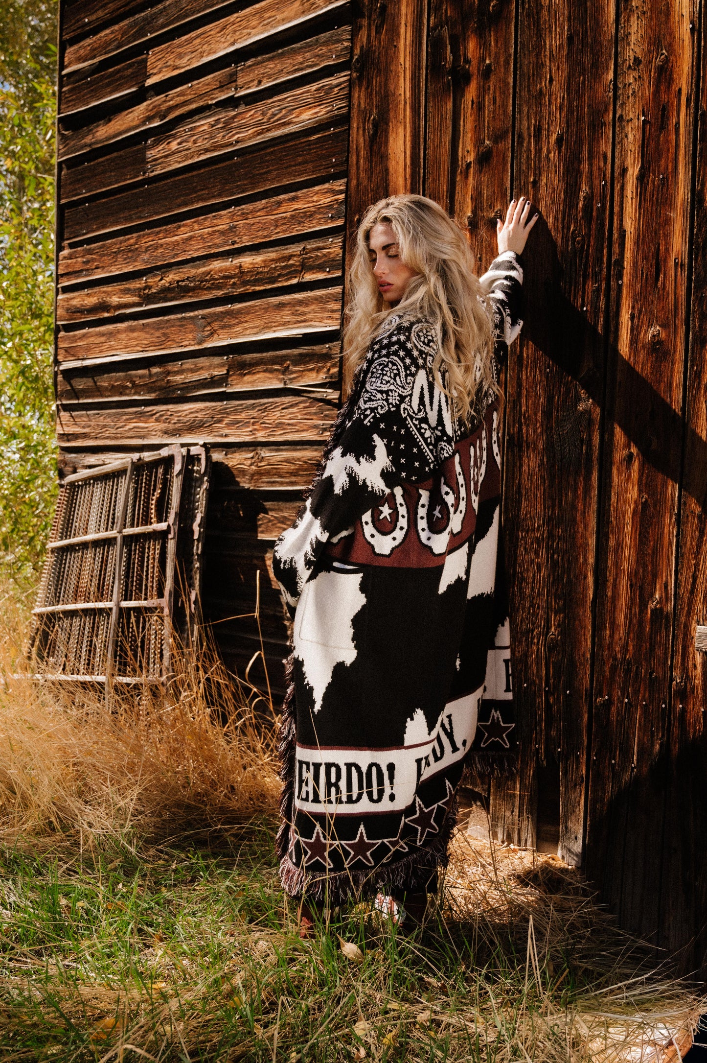 Person wearing a patterned outfit standing in front of a wooden building.