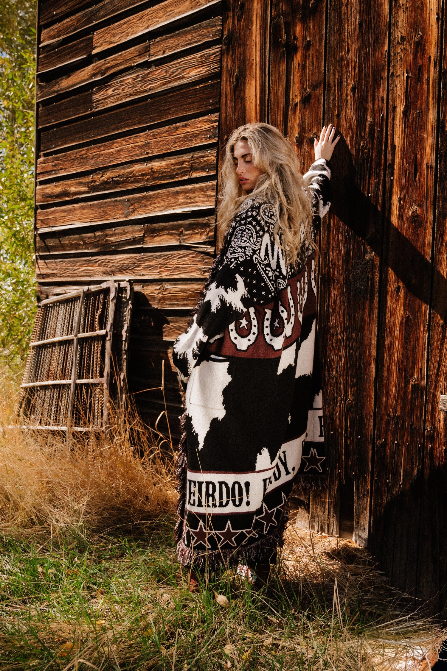 Person wearing a patterned outfit standing in front of a wooden building.