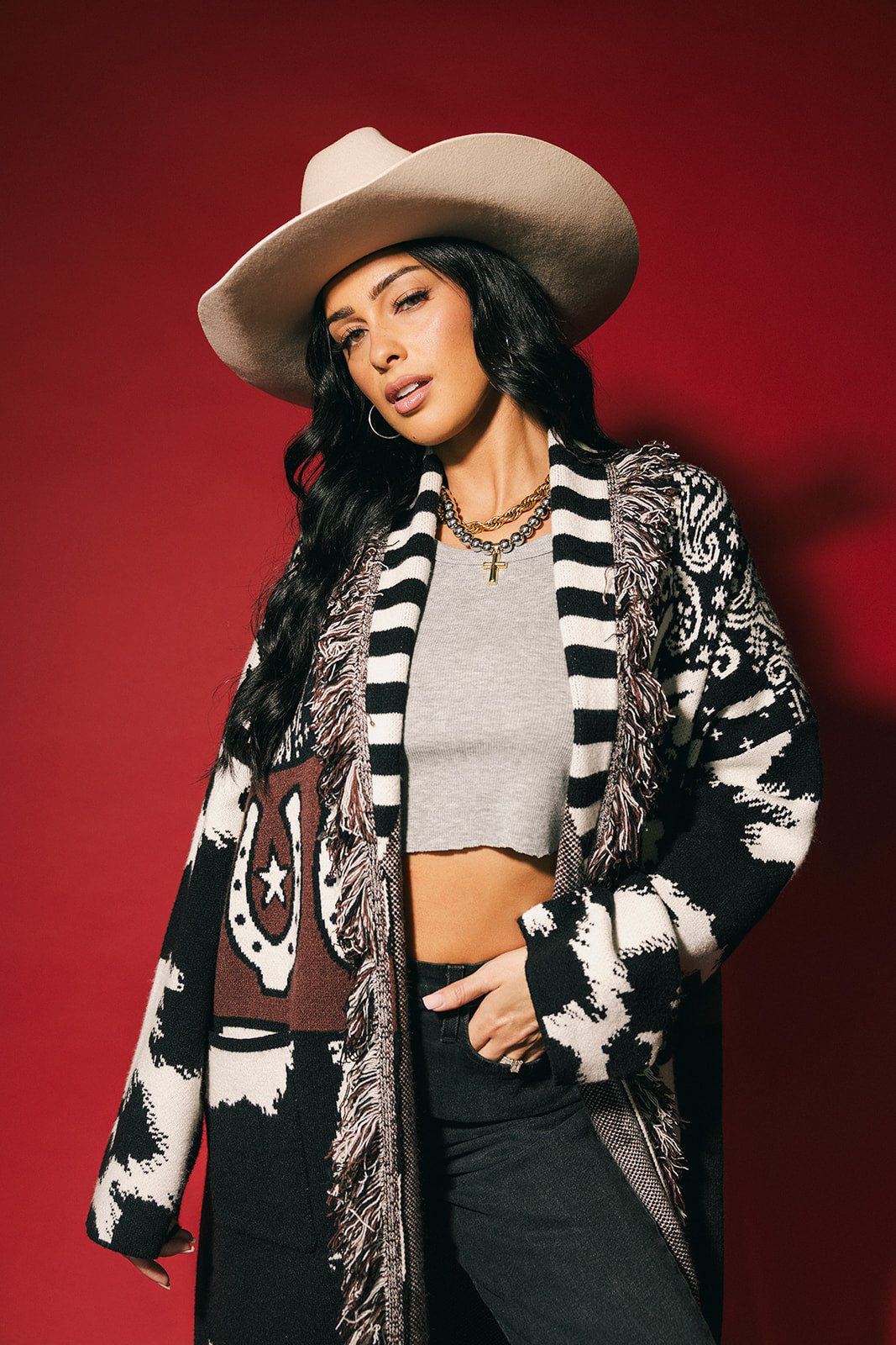 Woman wearing a cowboy hat and patterned cardigan against a red background