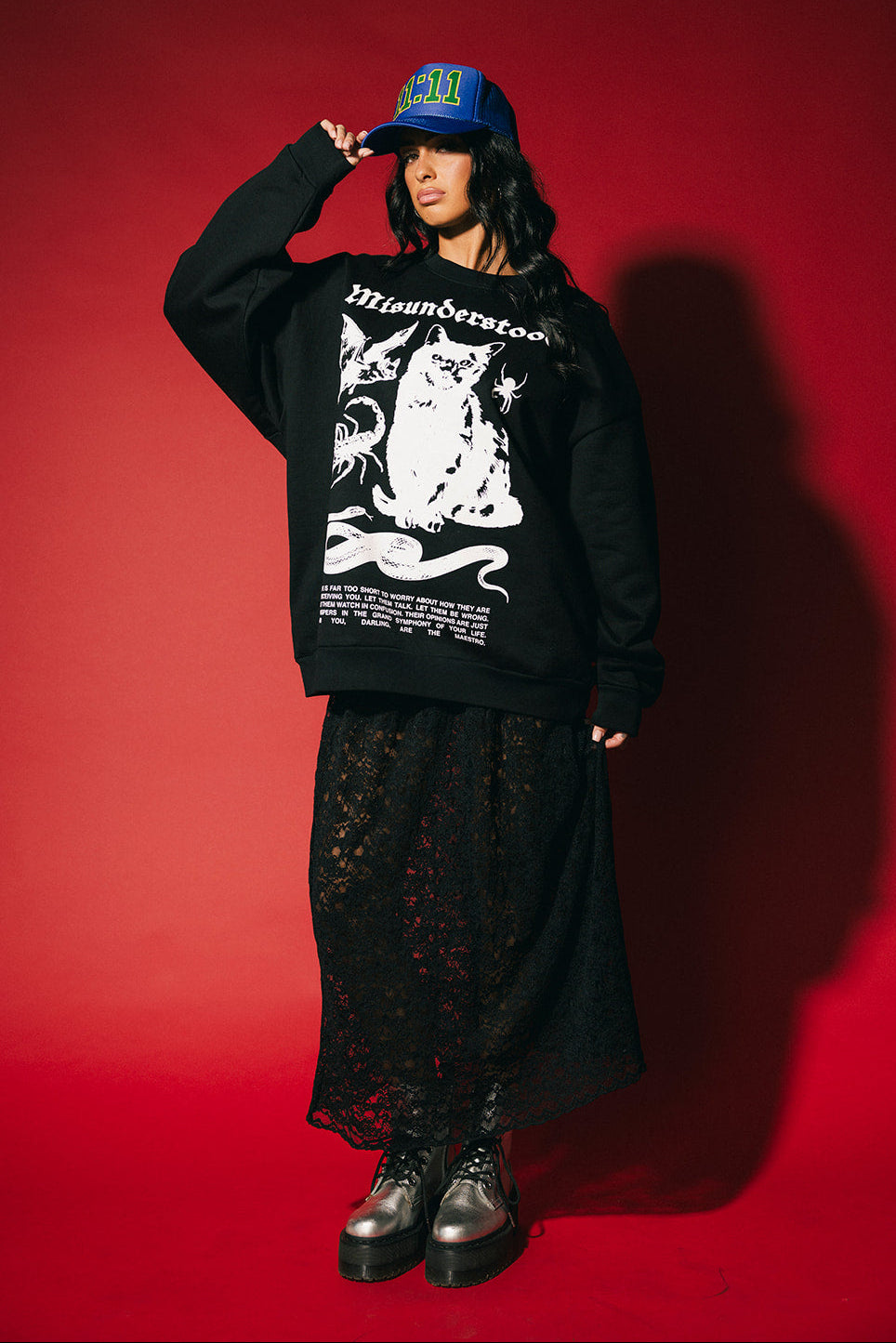 Person wearing a black sweatshirt with a graphic design, black pants, and a blue cap on a red background