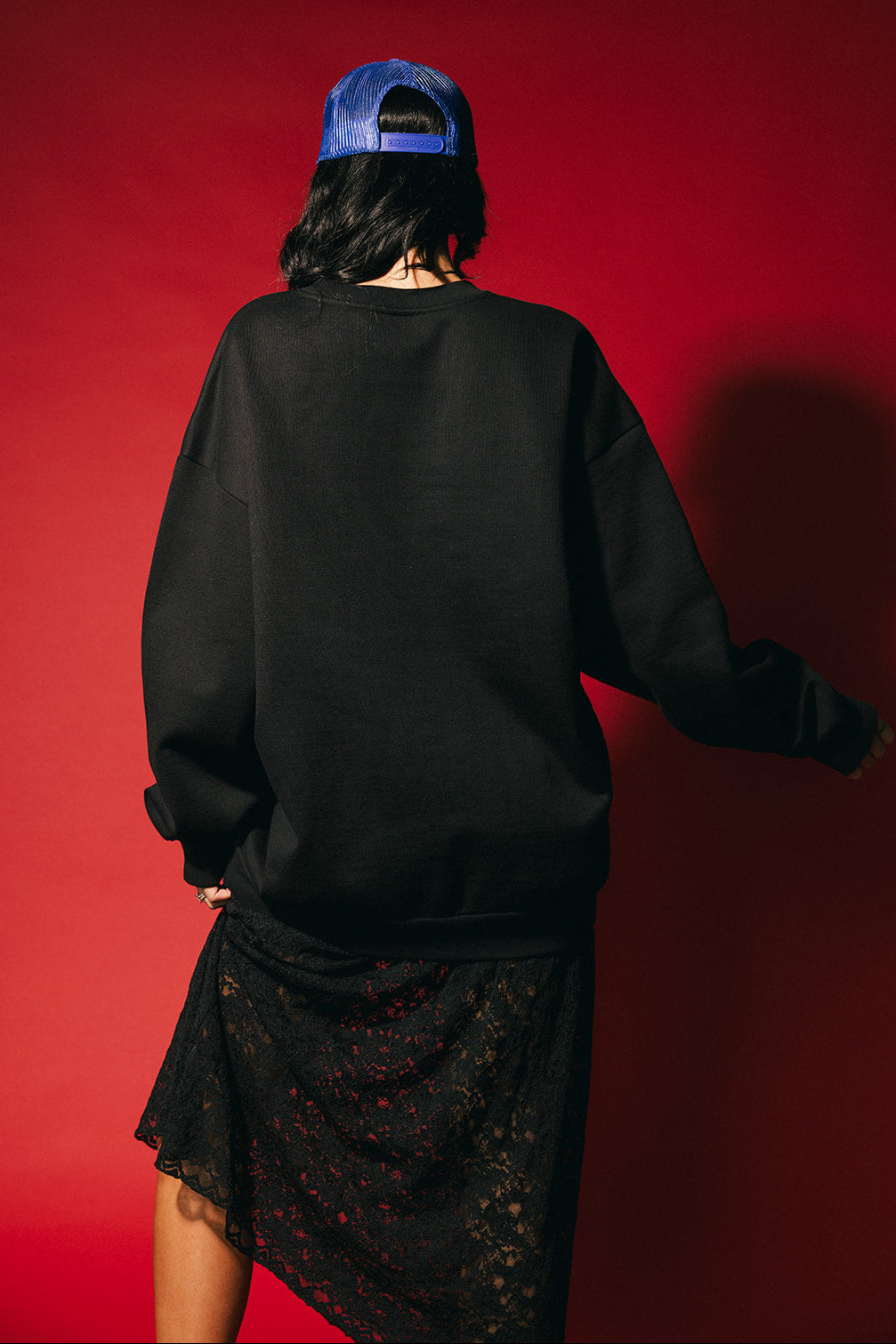 Person wearing a black sweatshirt and blue cap with a red background