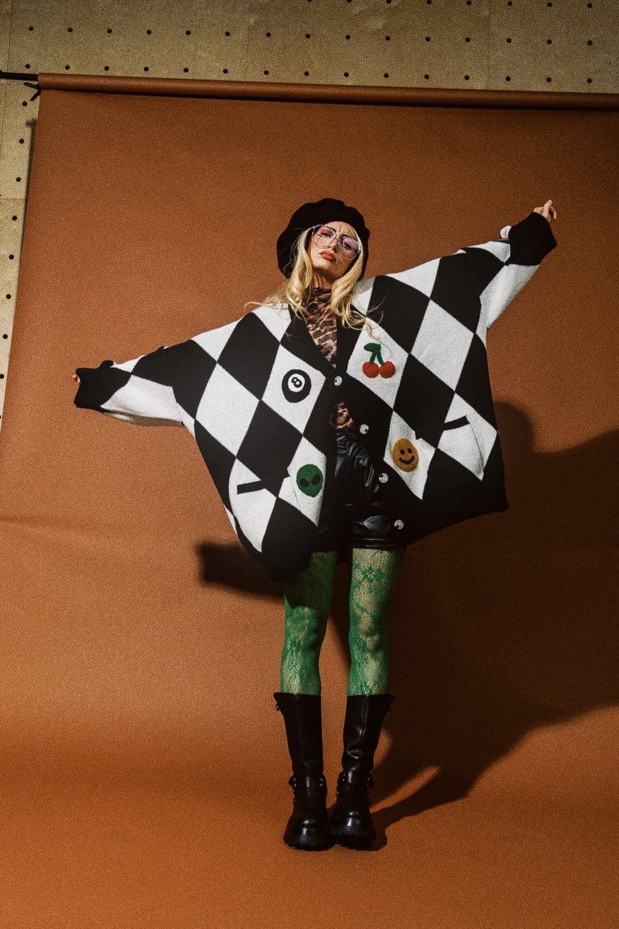 Person wearing a black and white checkered poncho with colorful buttons on a brown background