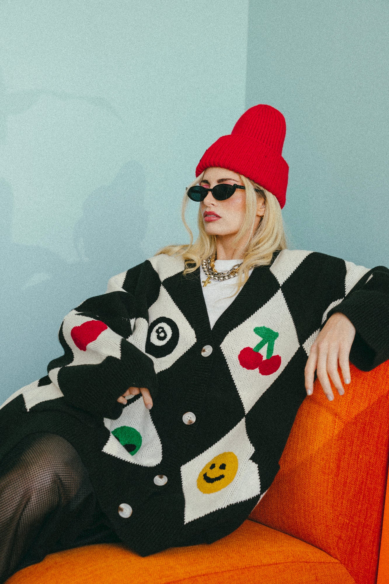 Person wearing a colorful cardigan with cartoon designs, sitting on an orange couch against a light blue wall.
