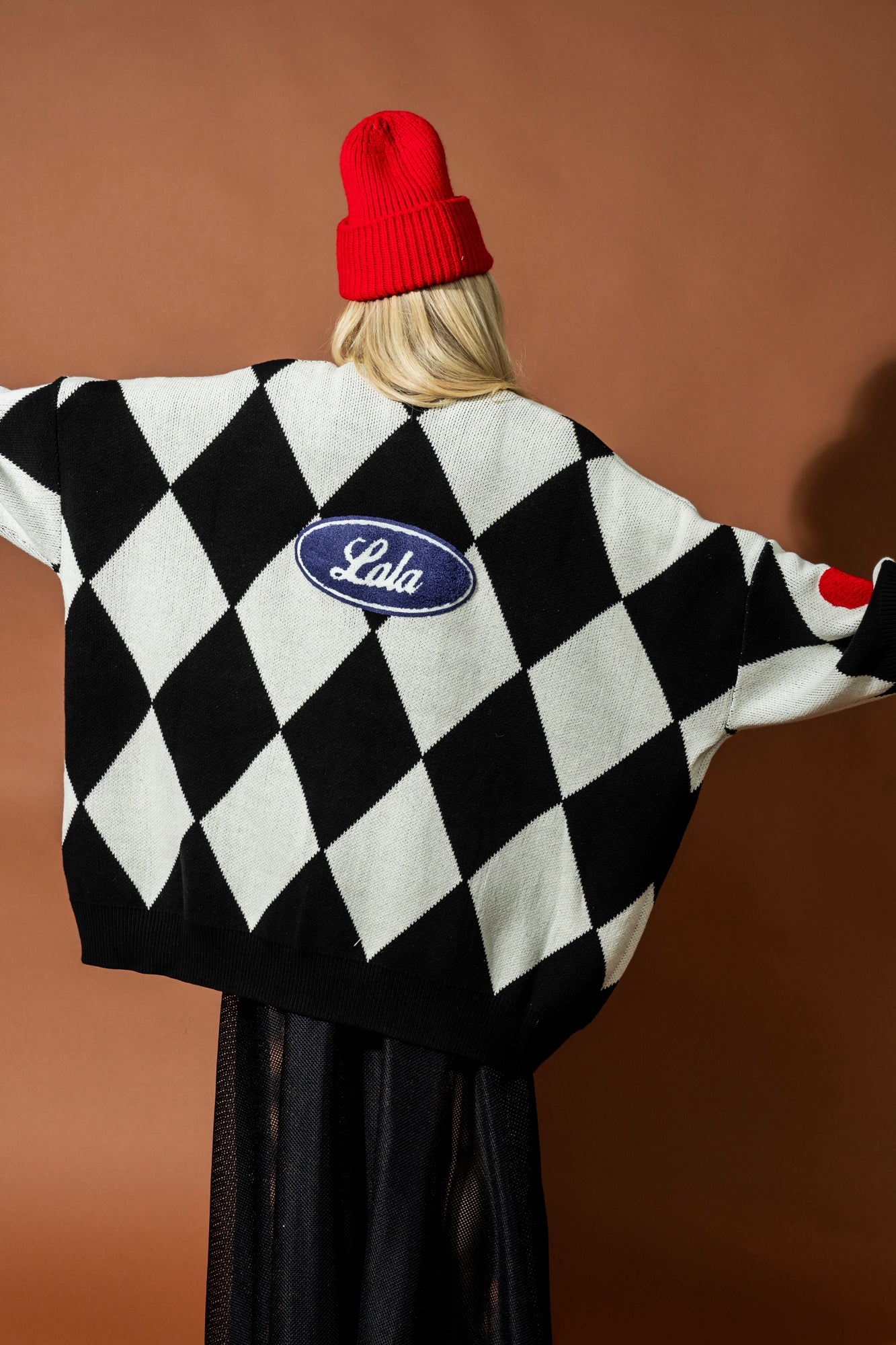 Person wearing a black and white checkered sweater with a visible brand logo on a brown background