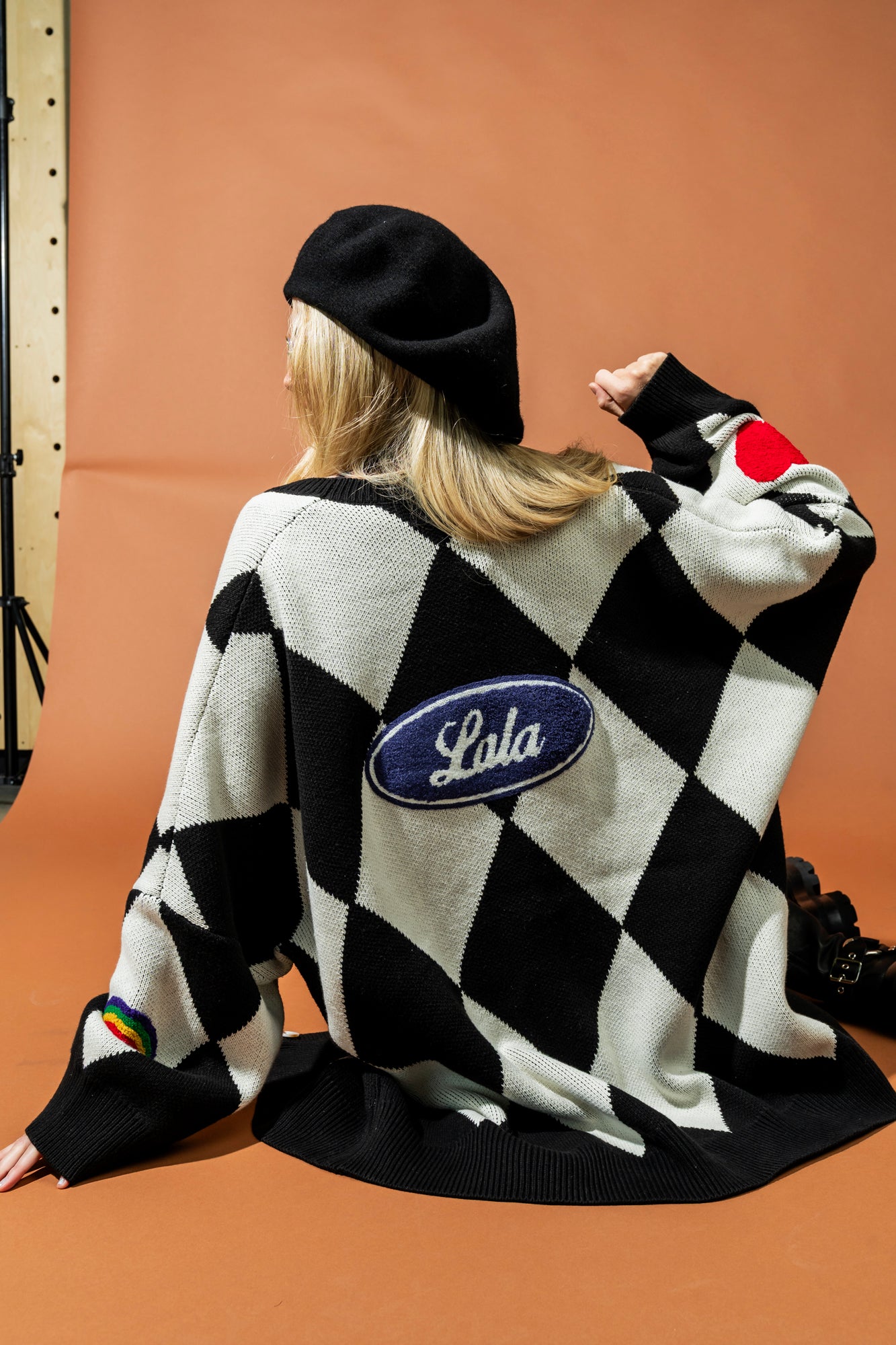 Person wearing a black and white checkered sweater with 'Lala' logo on a brown background