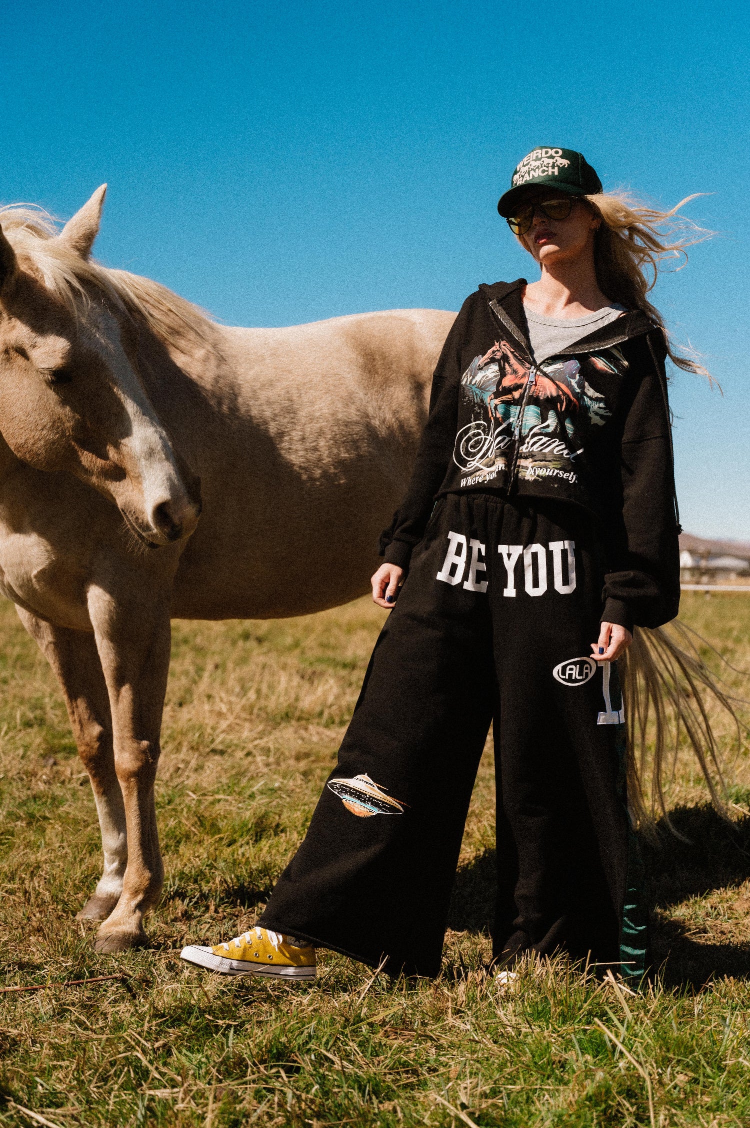 Person standing in a field wearing a black sweatsuit with a horse