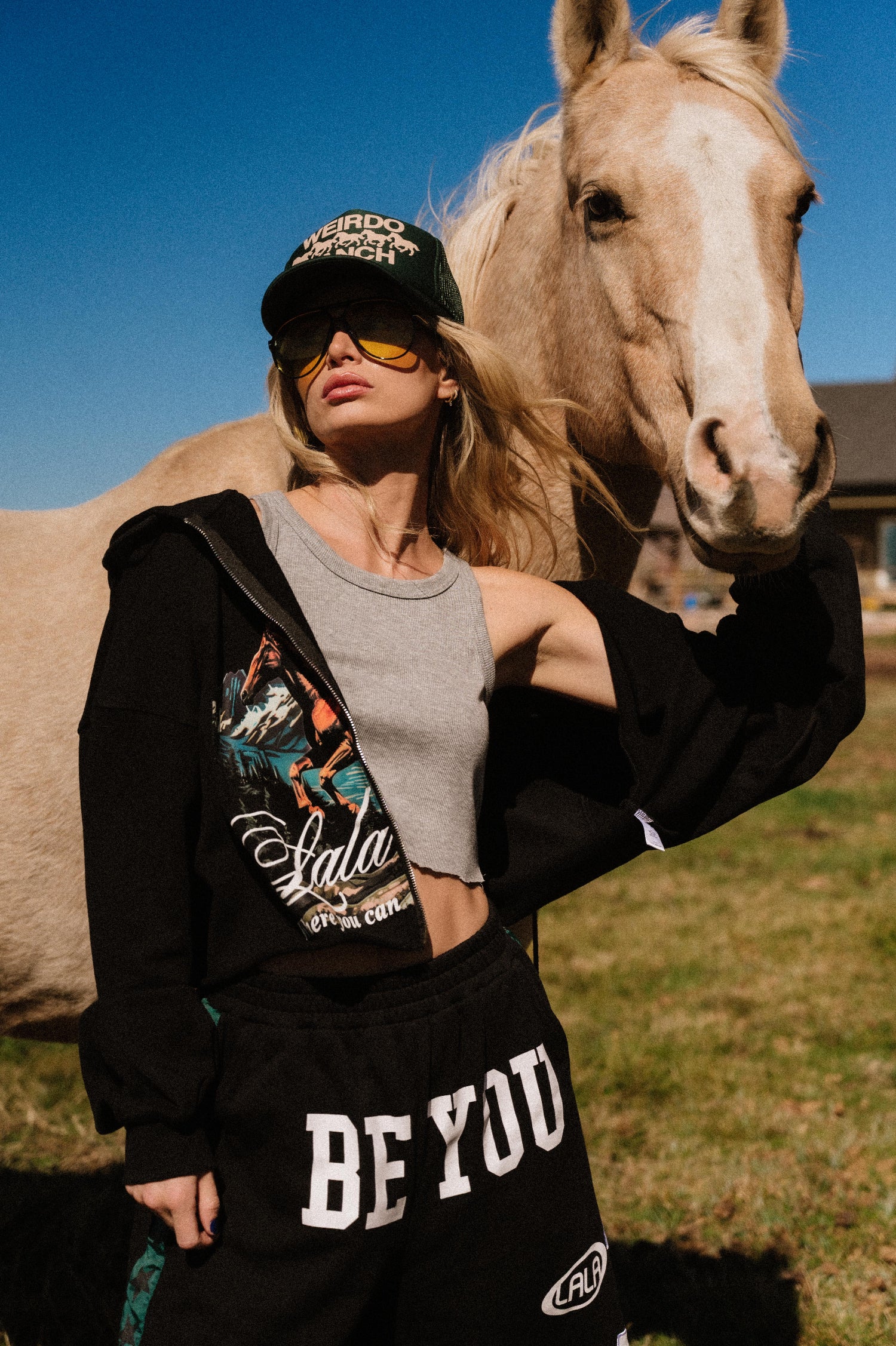 Person standing in a field wearing a sweatsuit with a horse