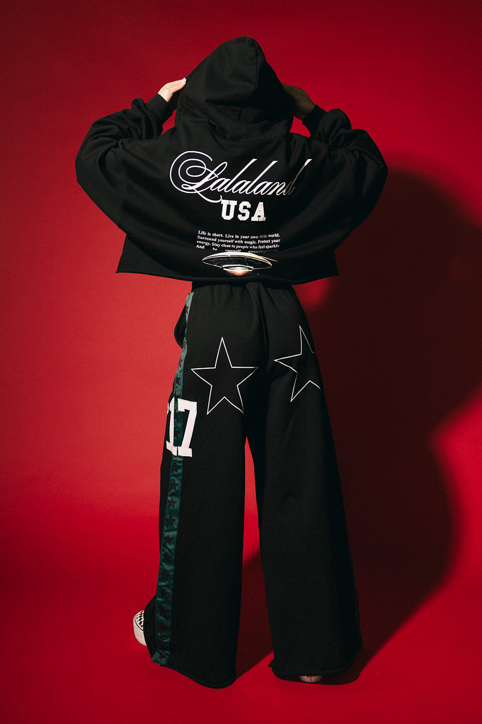 Person wearing a black hoodie and pants with visible branding on a red background