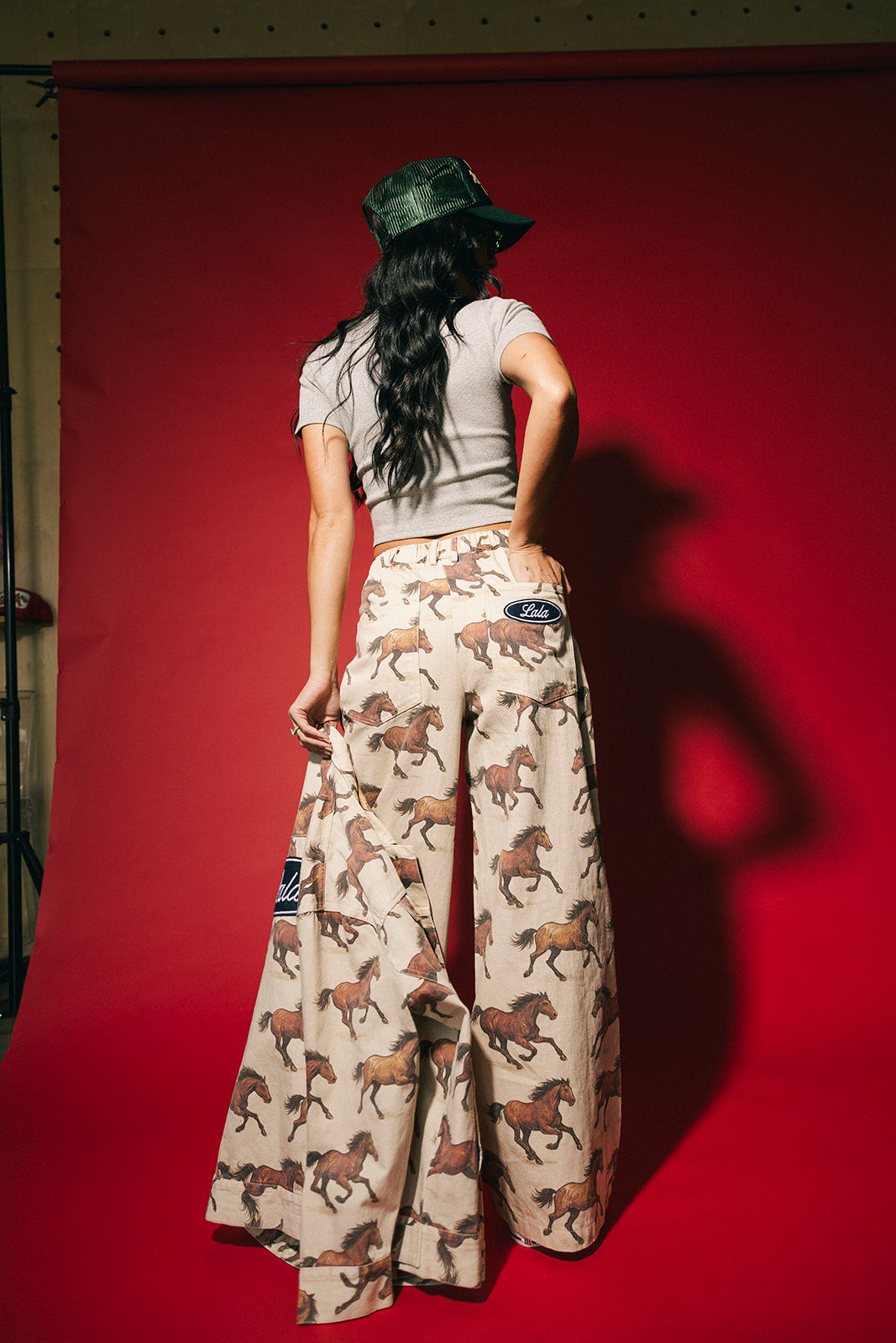 Person wearing a gray ribbed baby tee and horse-patterned pants against a red background
