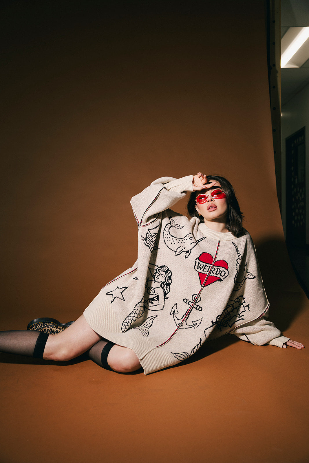 Woman wearing a patterned sweater sitting on the floor against a brown wall.