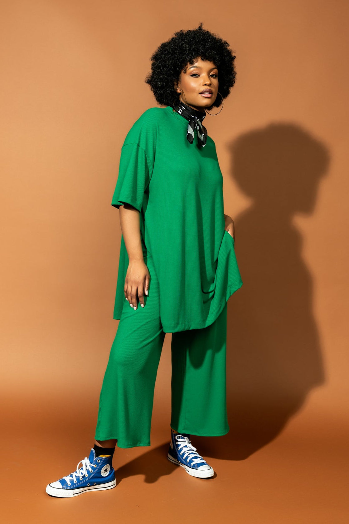 photo of girl wearing green ribbed matching set. The top is long and oversized with high side slits. Pants are cropped and wide leg with an elastic waistband.