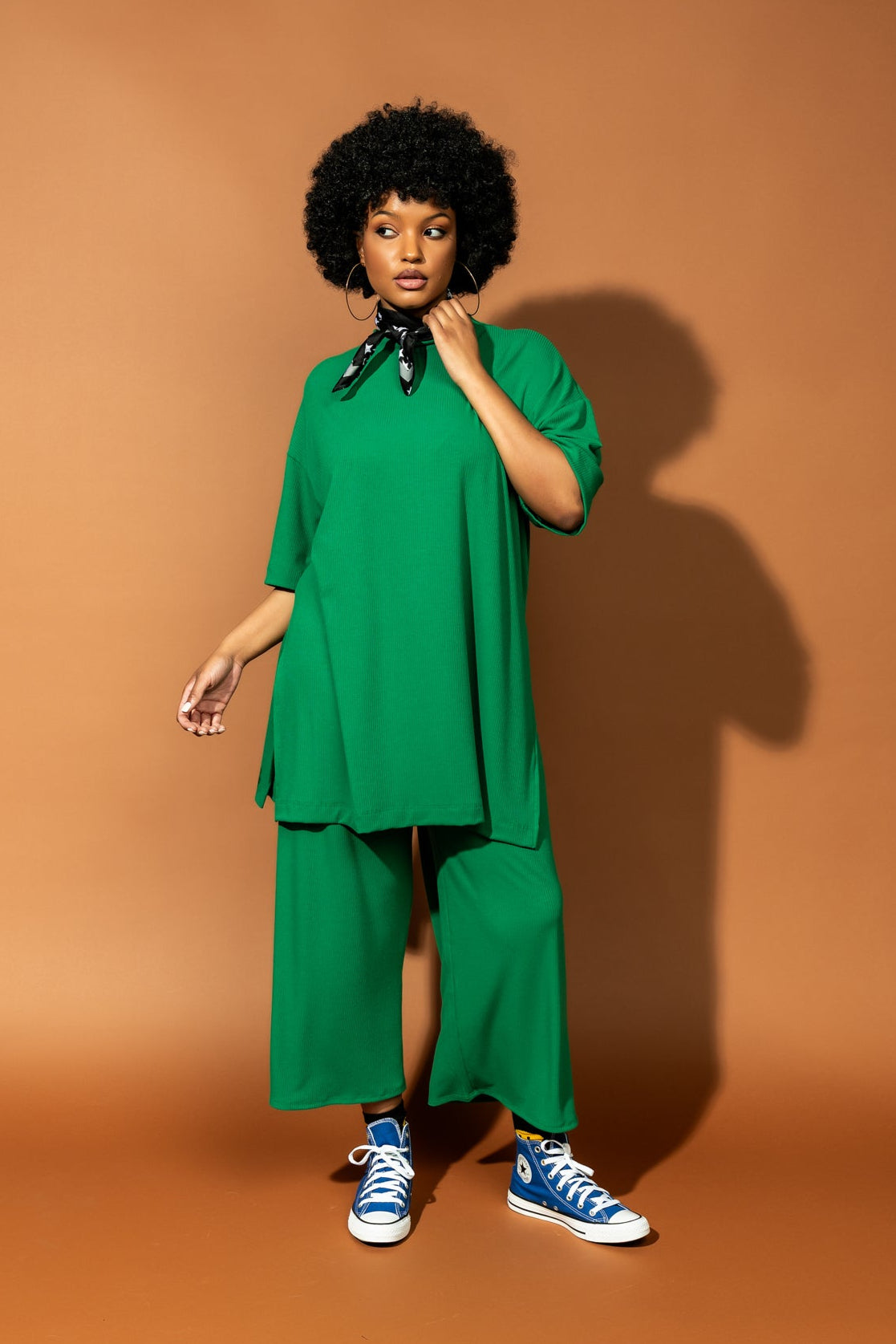 photo of girl wearing green ribbed matching set. The top is long and oversized with high side slits. Pants are cropped and wide leg with an elastic waistband.