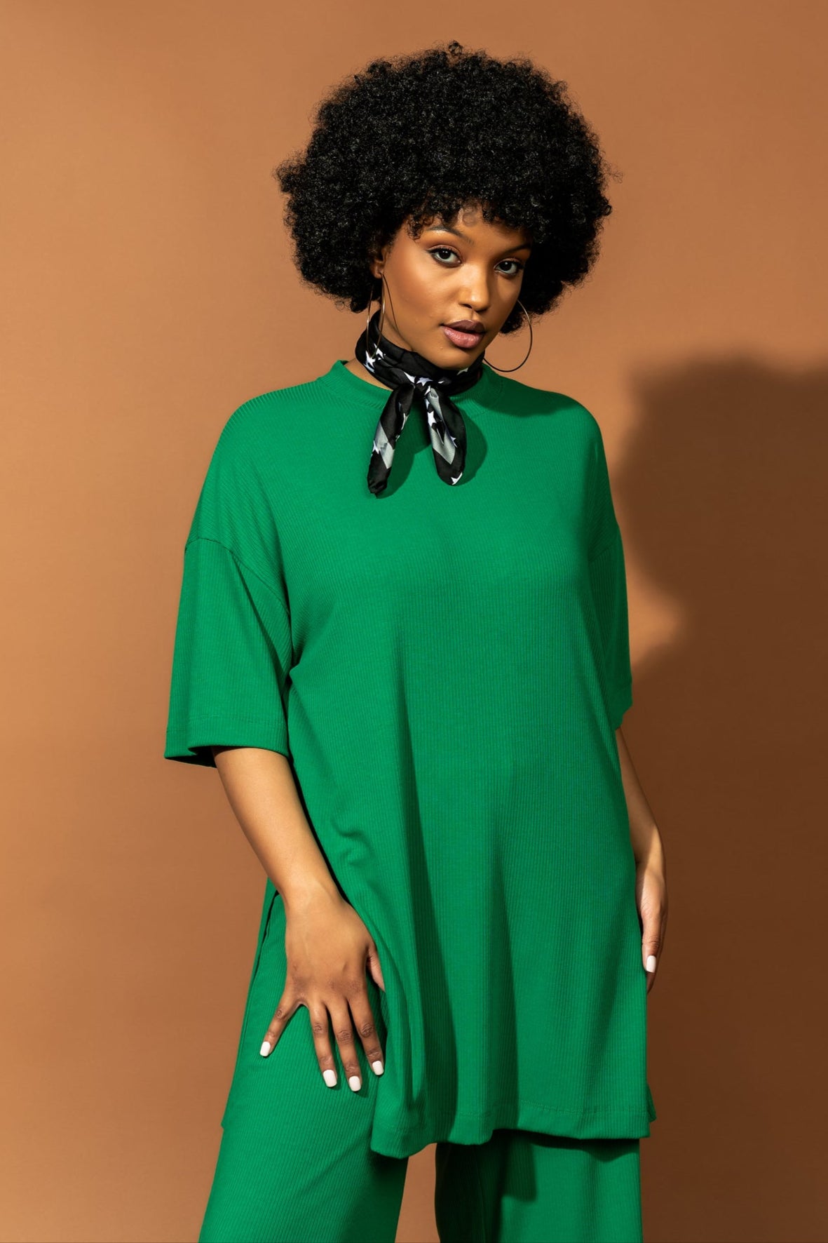 photo of girl wearing green ribbed matching set. The top is long and oversized with high side slits. Pants are cropped and wide leg with an elastic waistband.