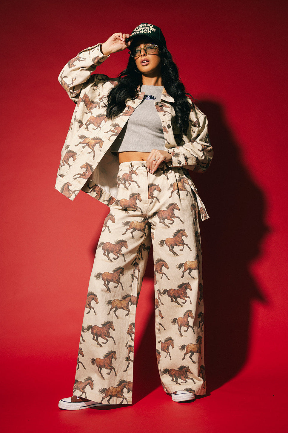 Person wearing white denim wide leg trousers with a horse pattern on a red background
