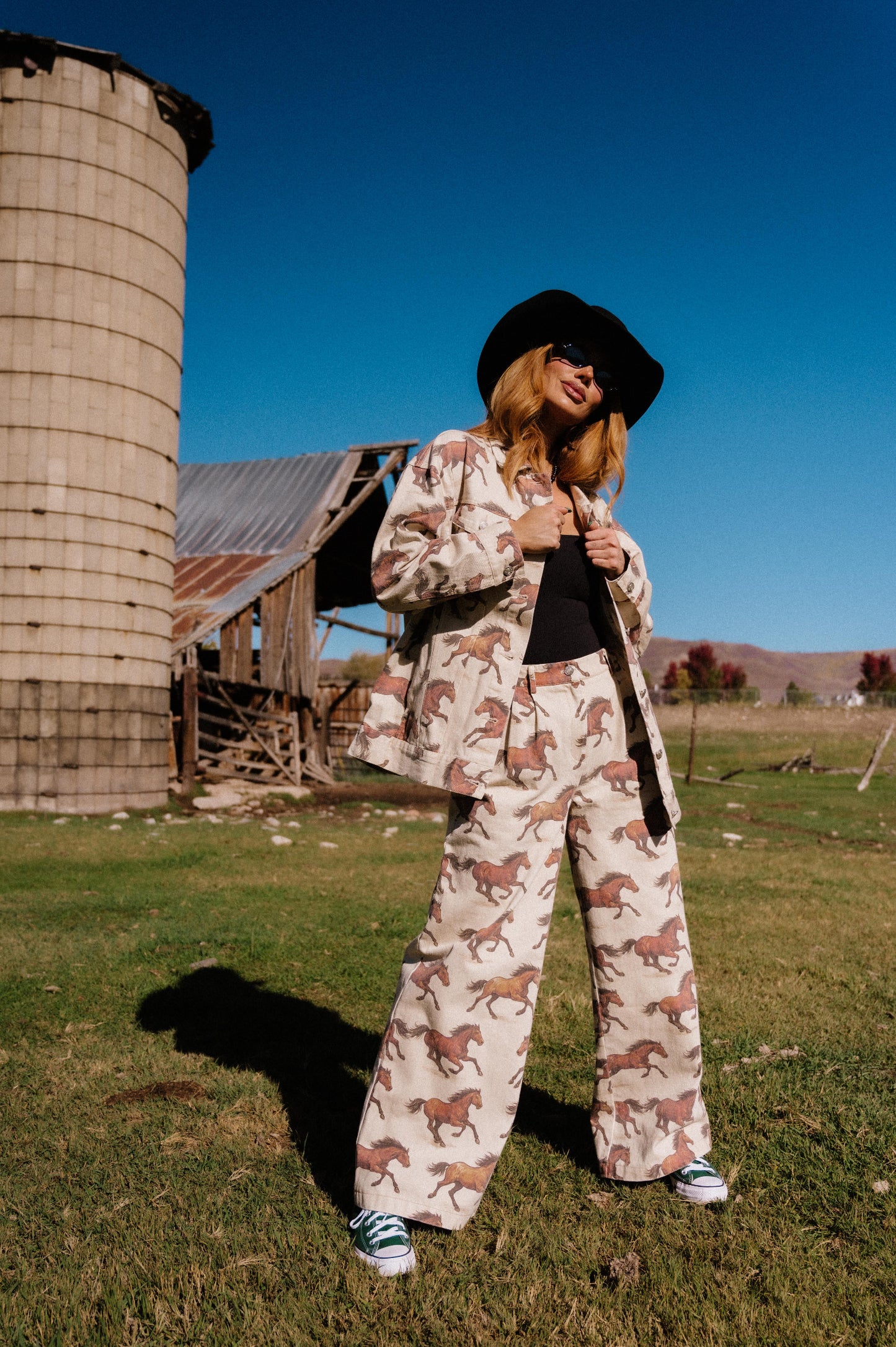 Person wearing white denim wide leg trousers with a horse pattern in front of a silo and barn.
