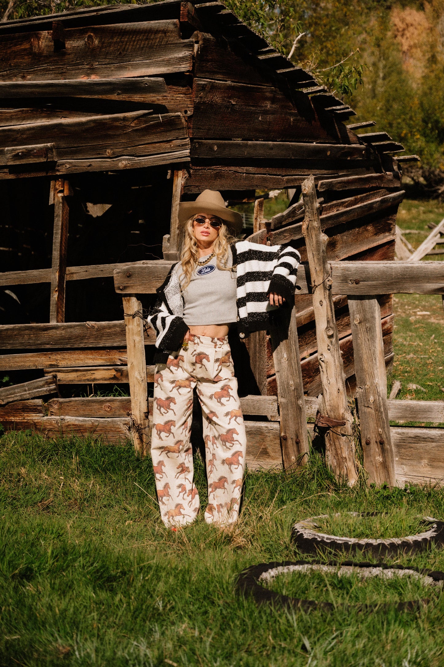 Person wearing white denim wide leg trousers with a horse pattern standing in front of an old wooden building.