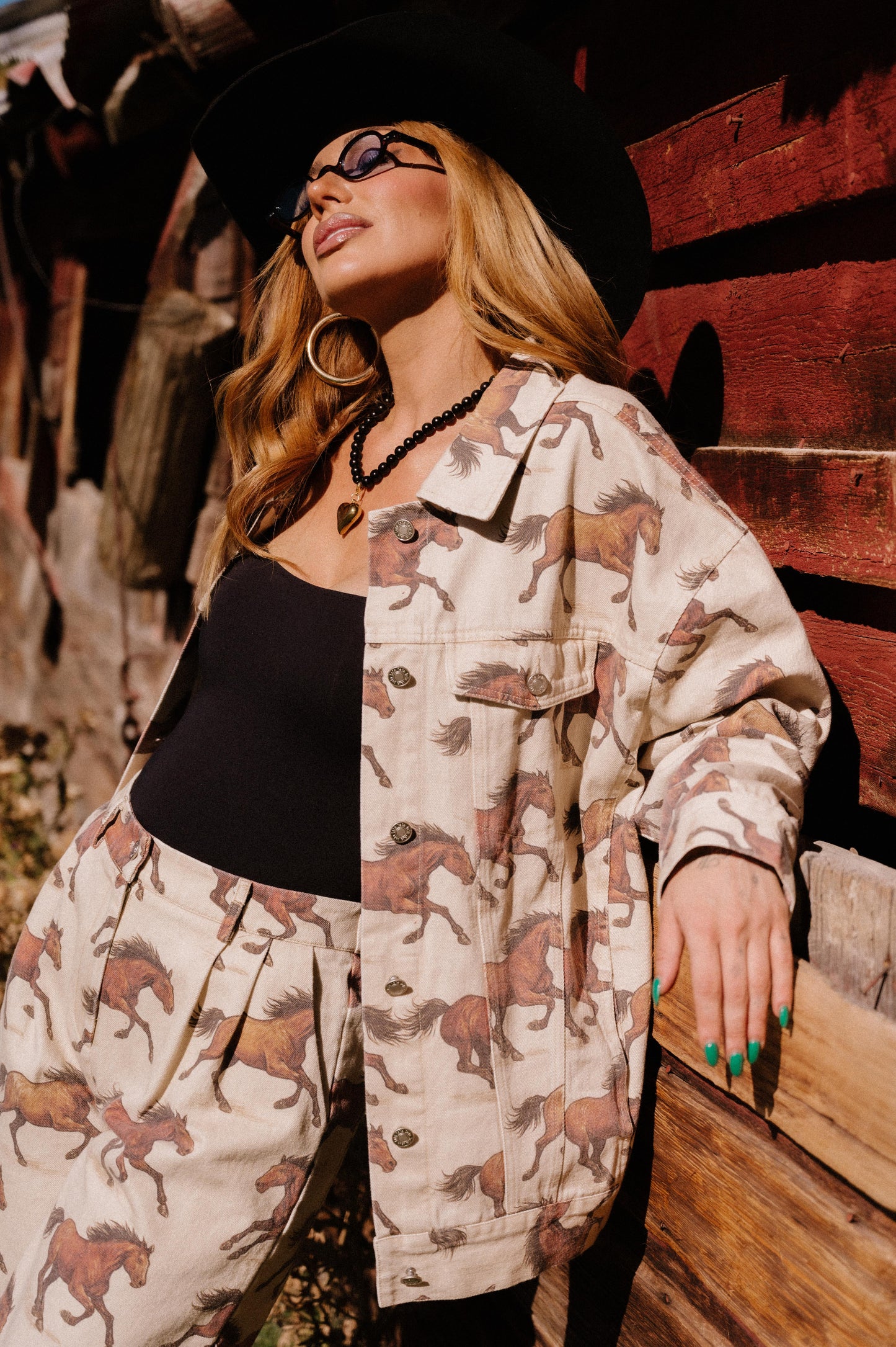 Woman wearing a white denim jacket with a horse pattern in front of a wooden wall.