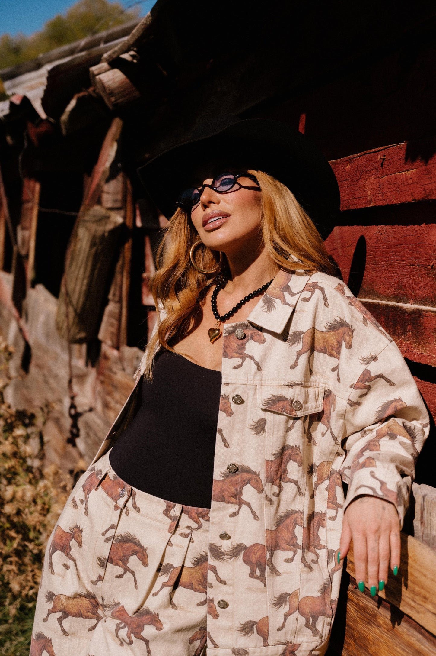 Woman wearing a white denim jacket with a horse pattern standing in front of a wooden structure.