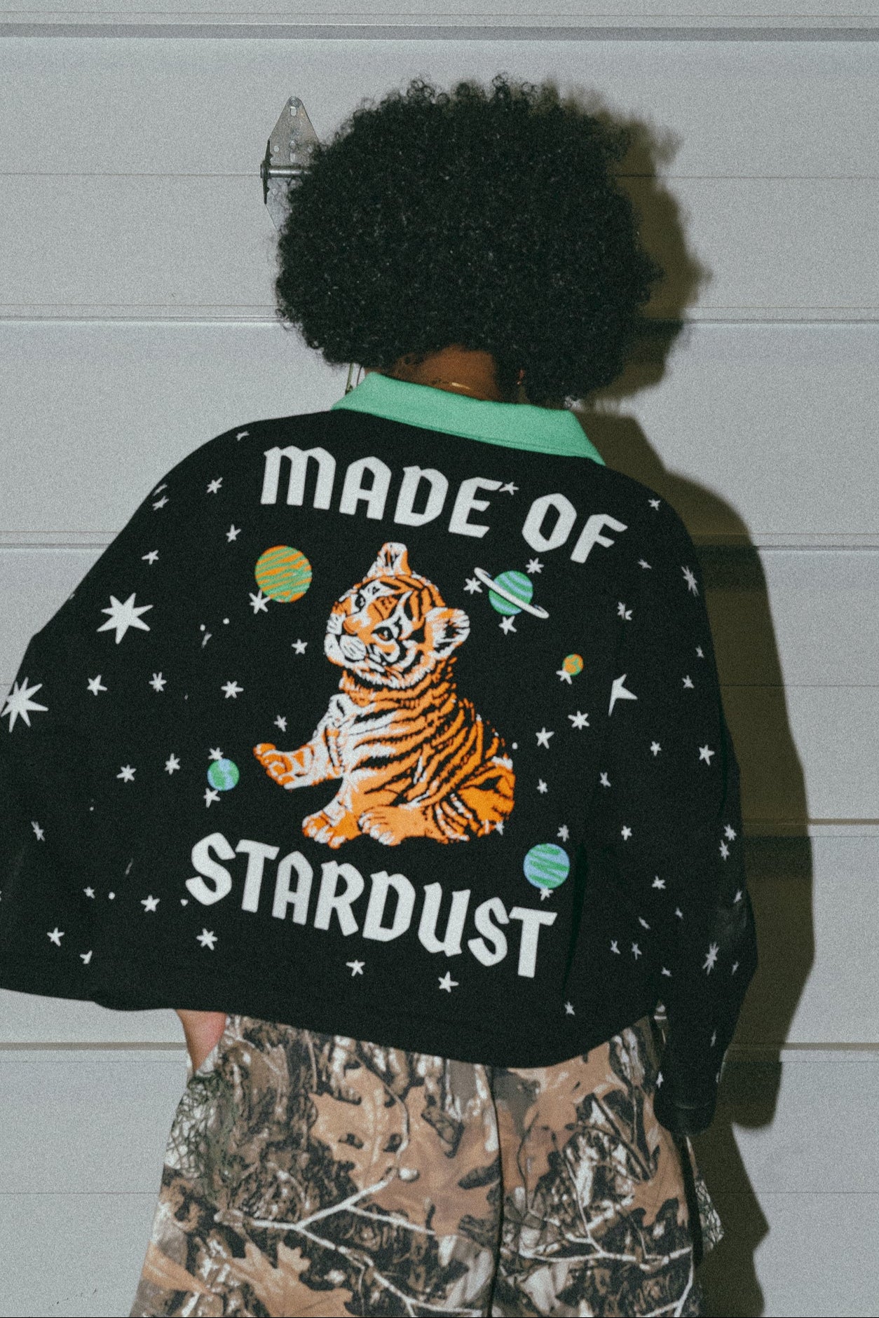 photo of girl wearing black cropped polo with green collar and white stars all over with baby tigers on the front and a baby tiger on the back words that say "made of stardust"