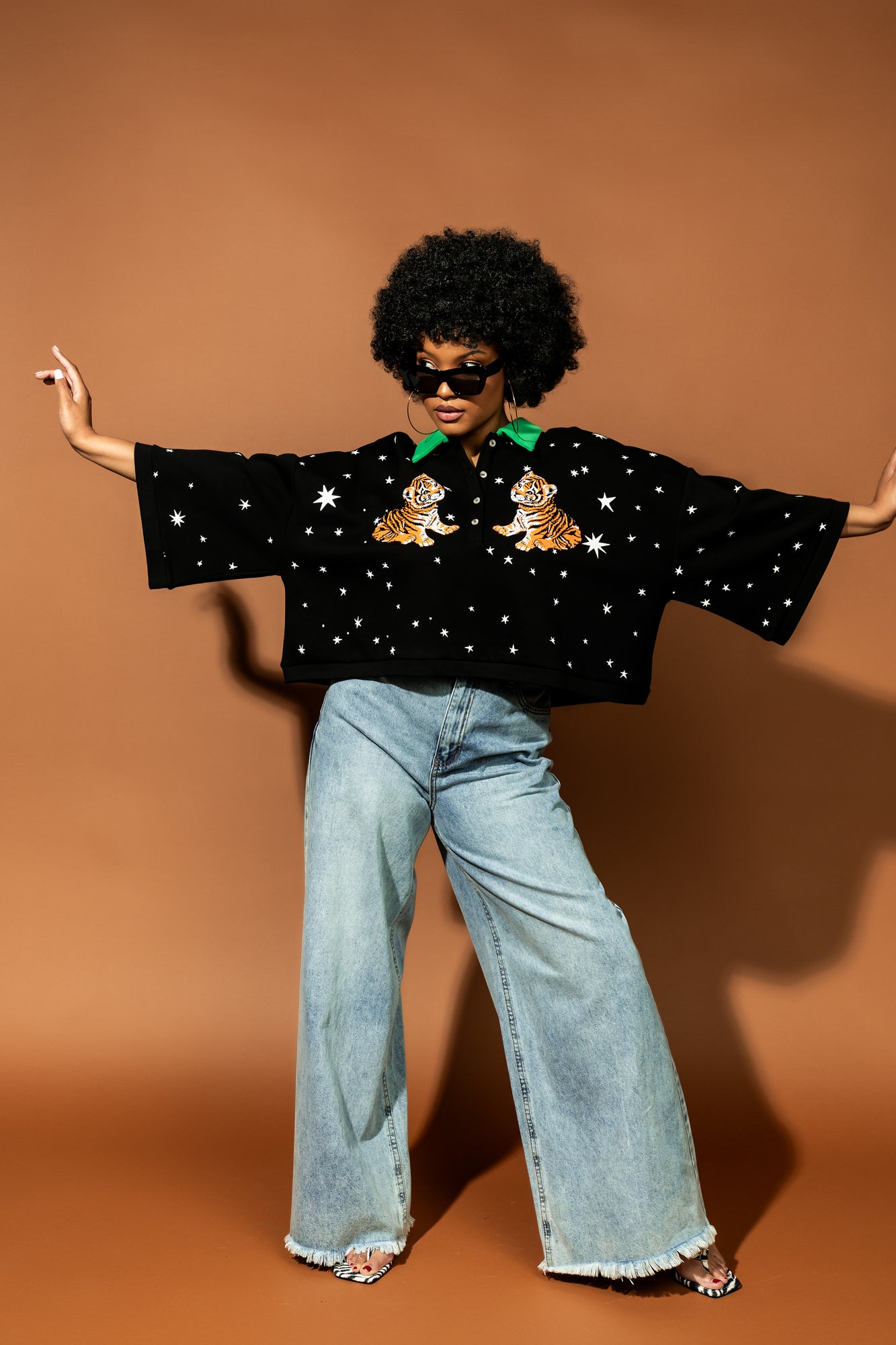 photo of girl wearing black cropped polo with green collar and white stars all over with baby tigers on the front and a baby tiger on the back words that say "made of stardust"