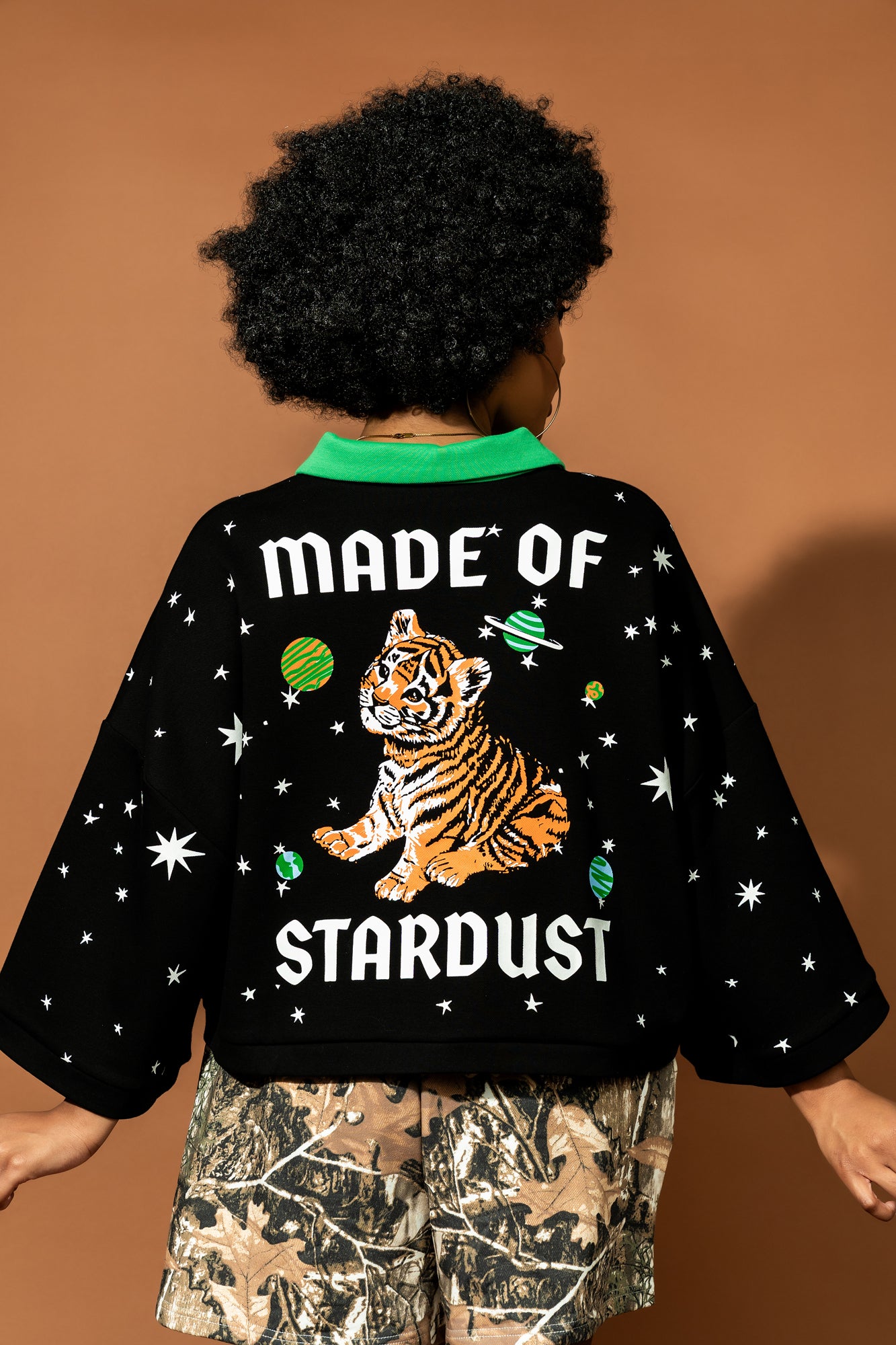 photo of girl wearing black cropped polo with green collar and white stars all over with baby tigers on the front and a baby tiger on the back words that say "made of stardust"